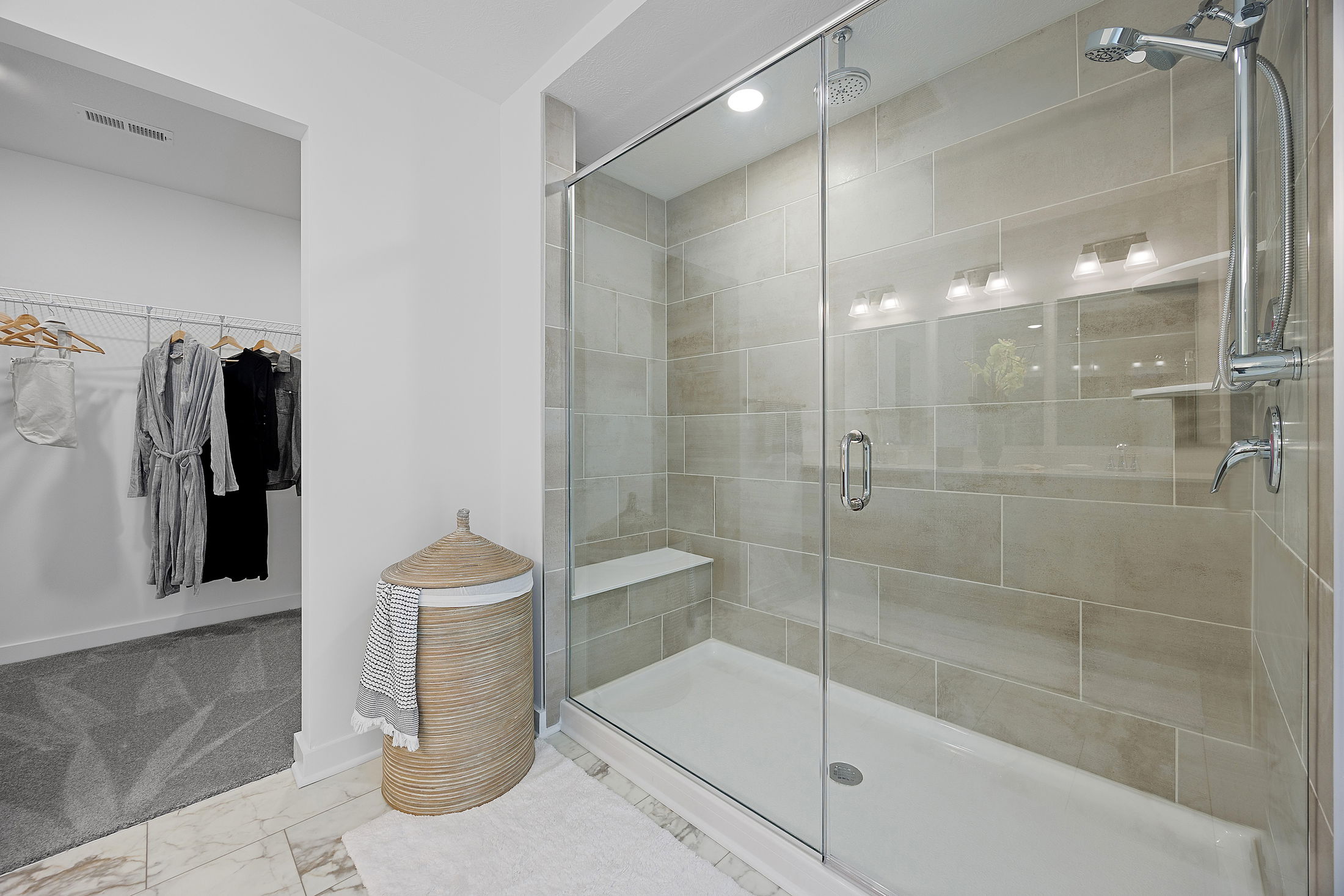 Modern bathroom featuring a spacious glass-enclosed shower with elegant tilework, adjacent to a walk-in closet.