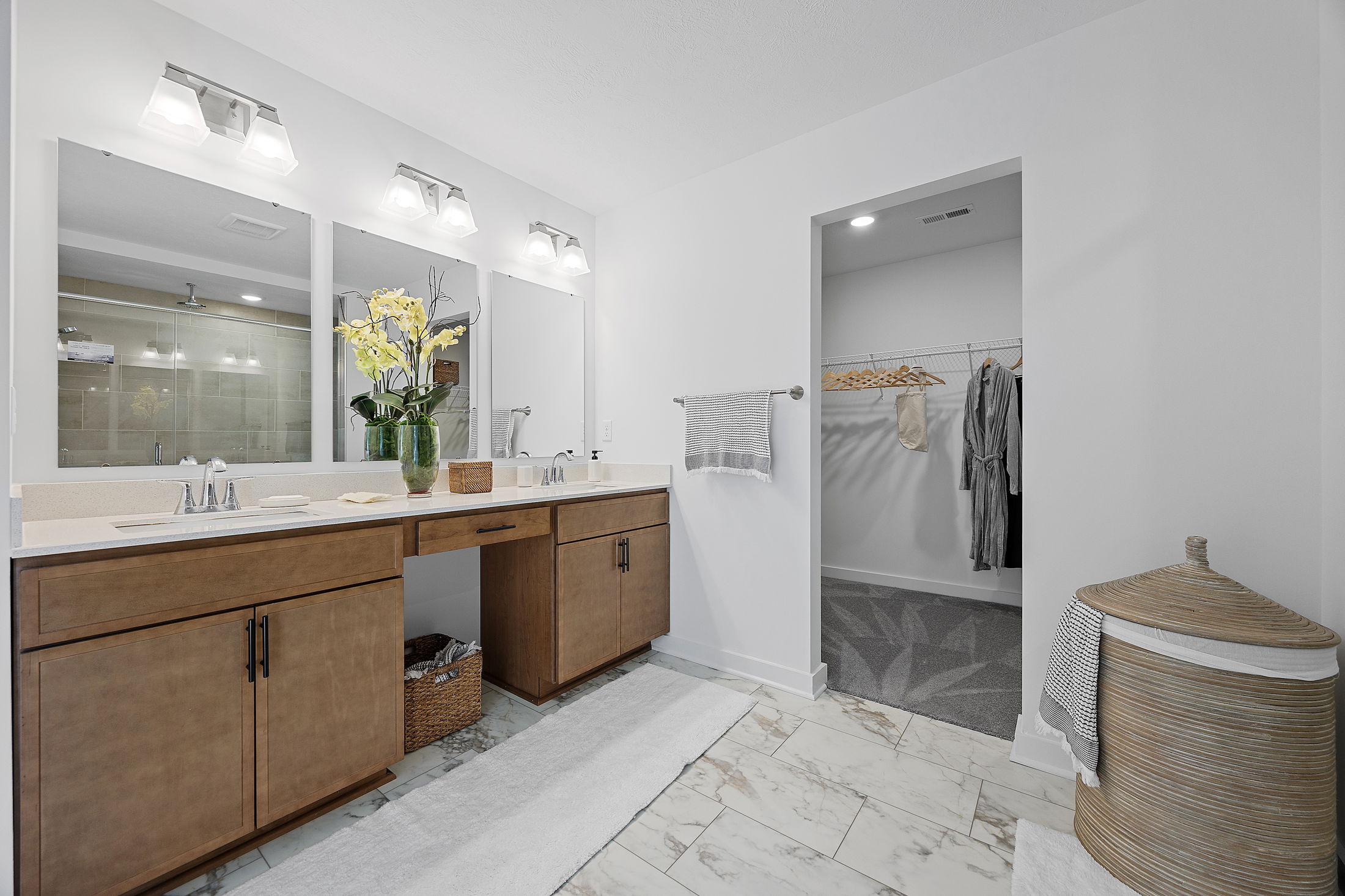 Elegant modern bathroom with double vanity, large mirrors, and walk-in closet featuring hanging robes.