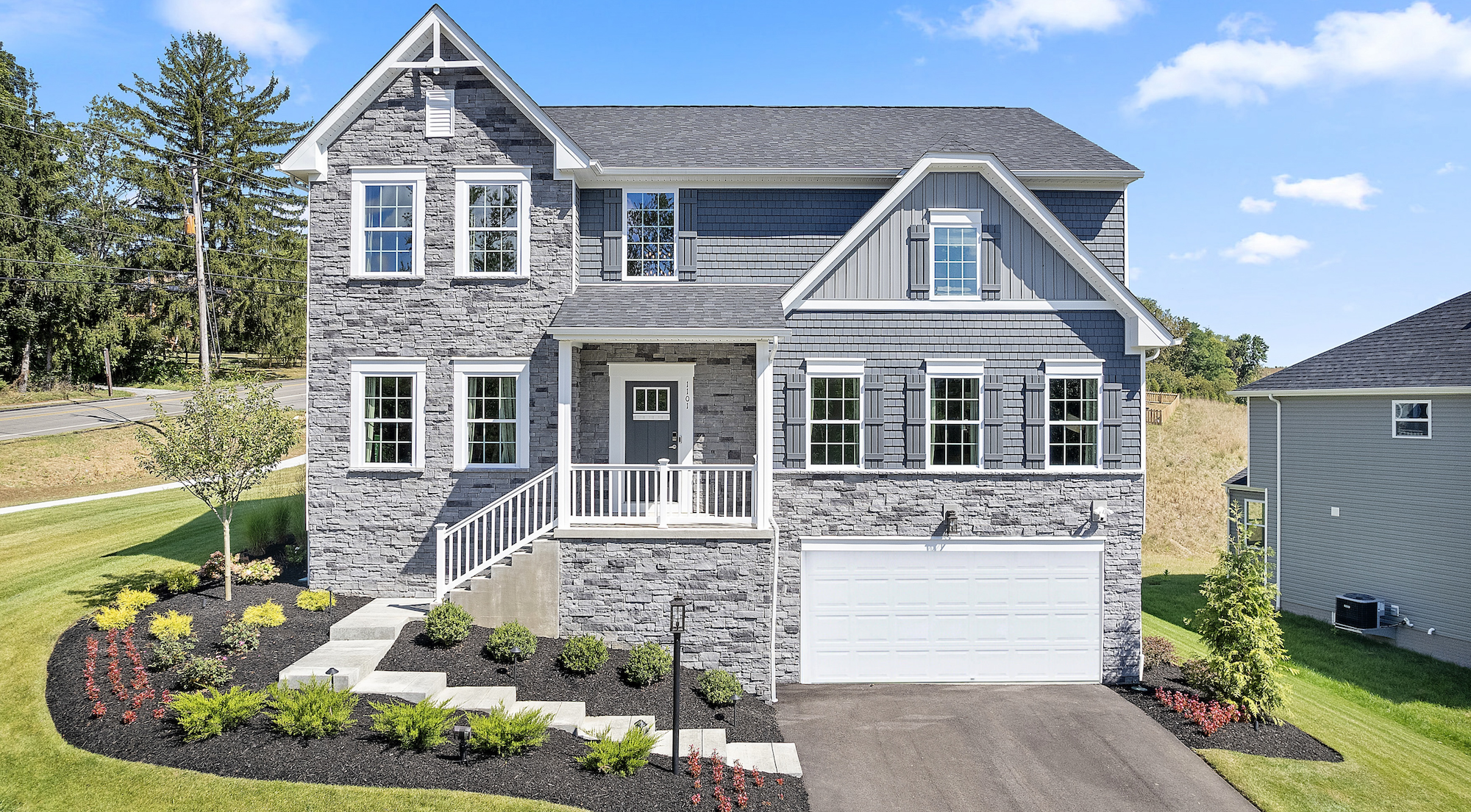 Front view of a modern two-story stone and siding house with a well-manicured lawn and attached garage, set against a clear blue sky.