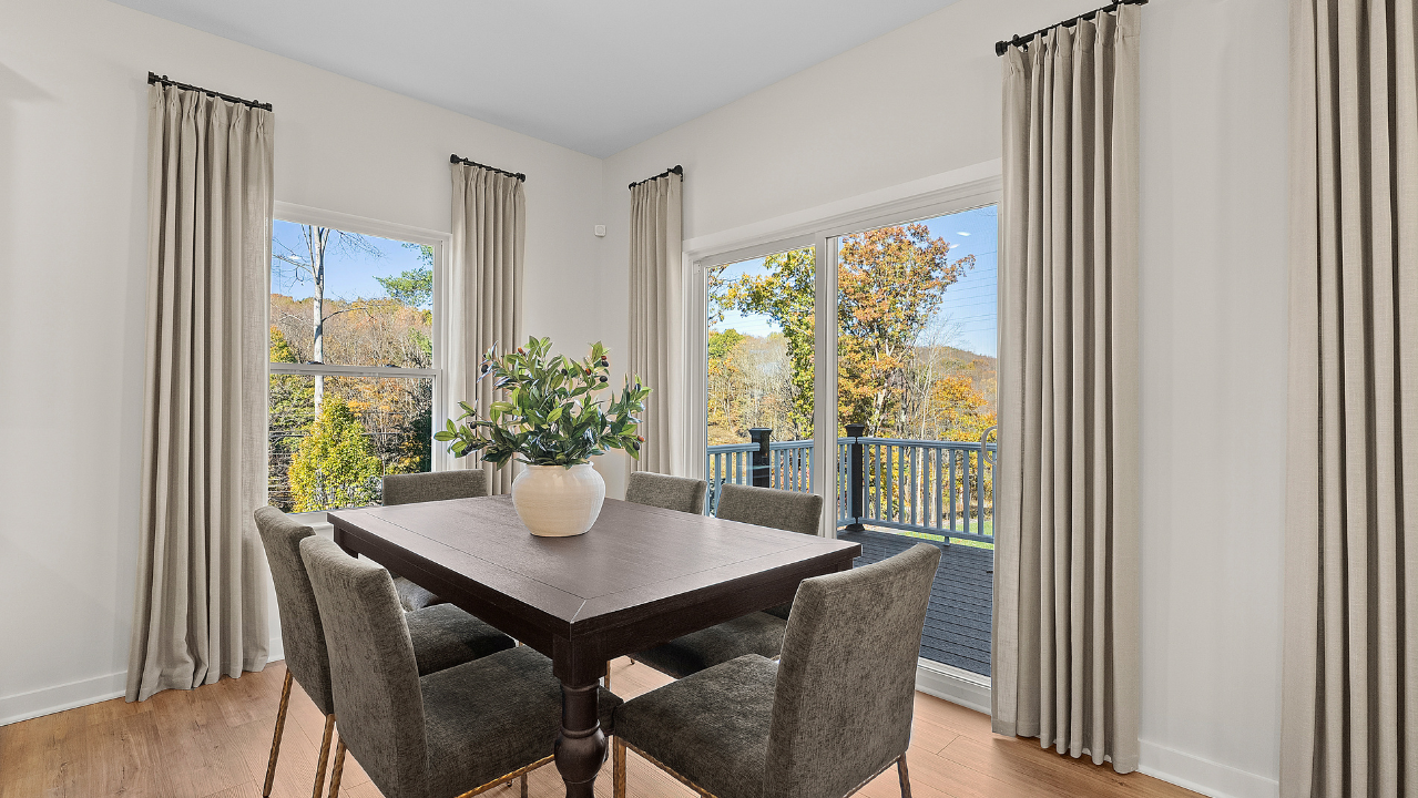 Modern dining room with a wooden table, upholstered chairs, and large windows offering a scenic outdoor view.