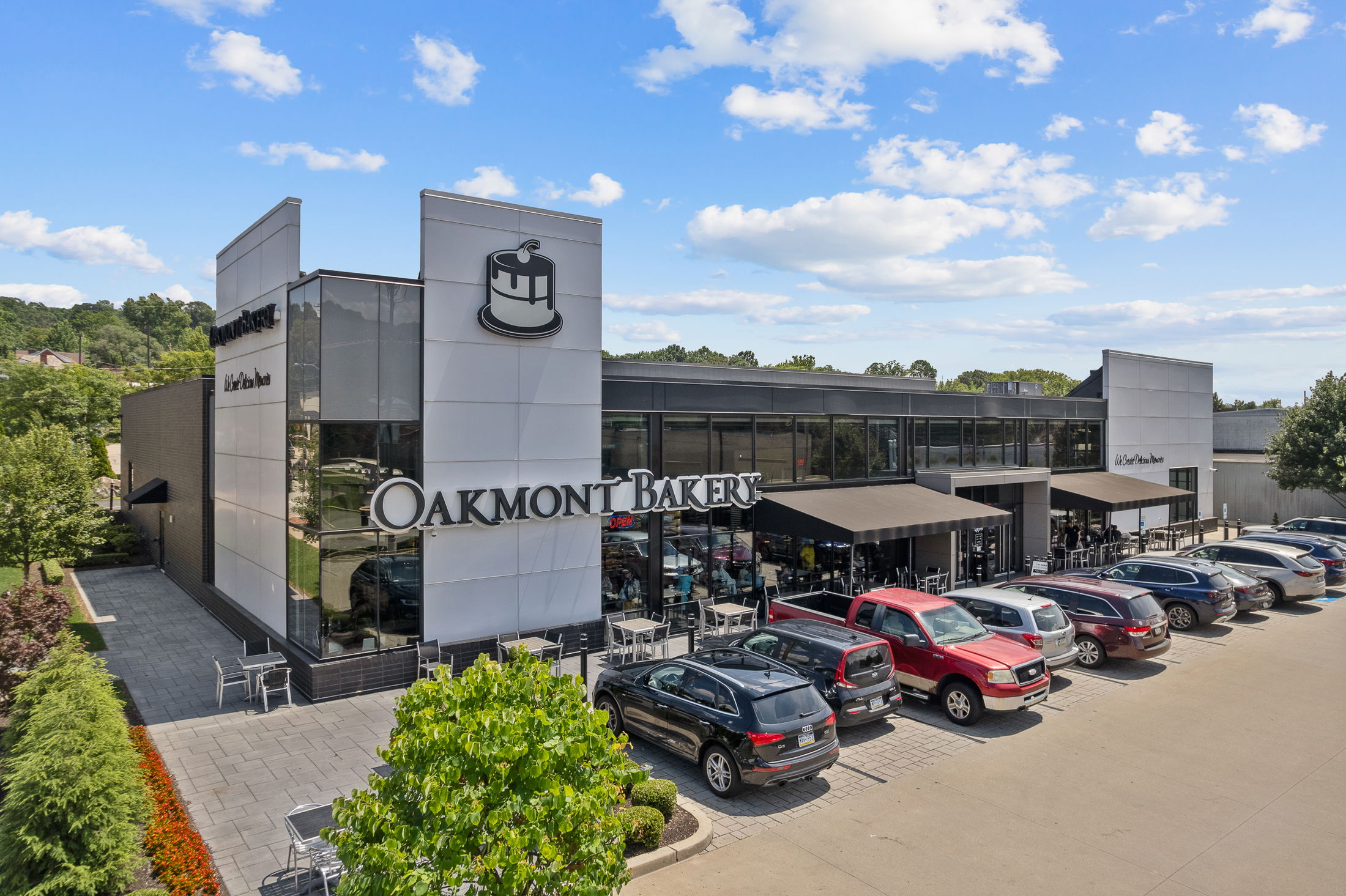 Modern exterior of Oakmont Bakery with parked cars and outdoor seating on a clear day.