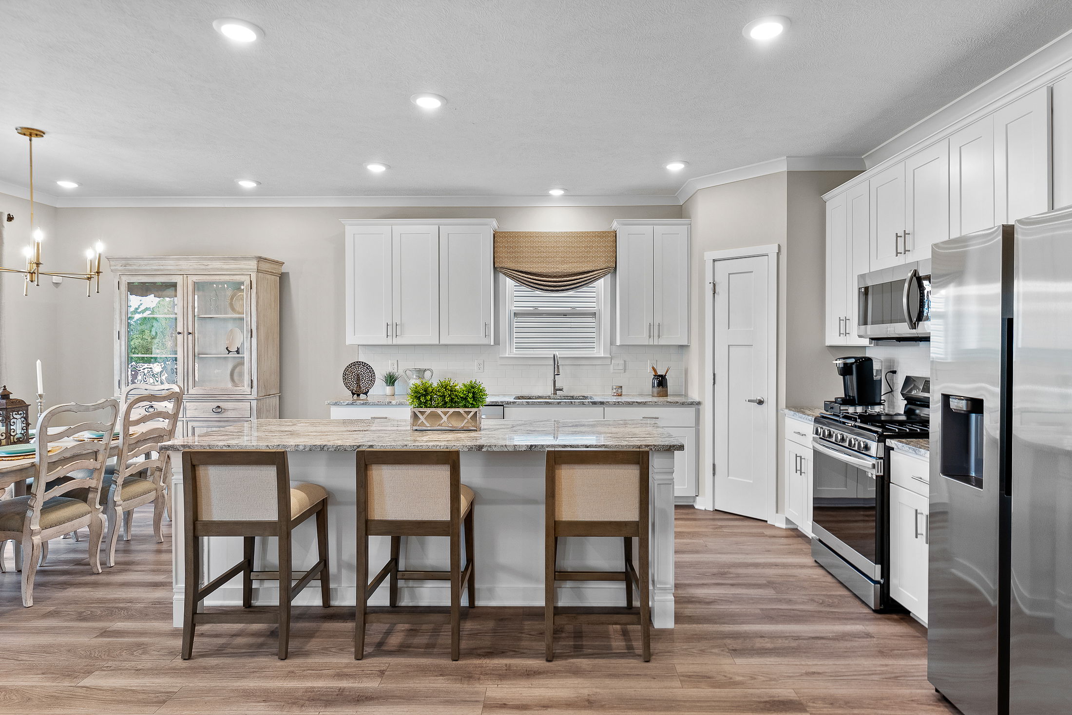 Modern kitchen with white cabinets, stainless steel appliances, and a central island with seating, adjacent to a dining area.