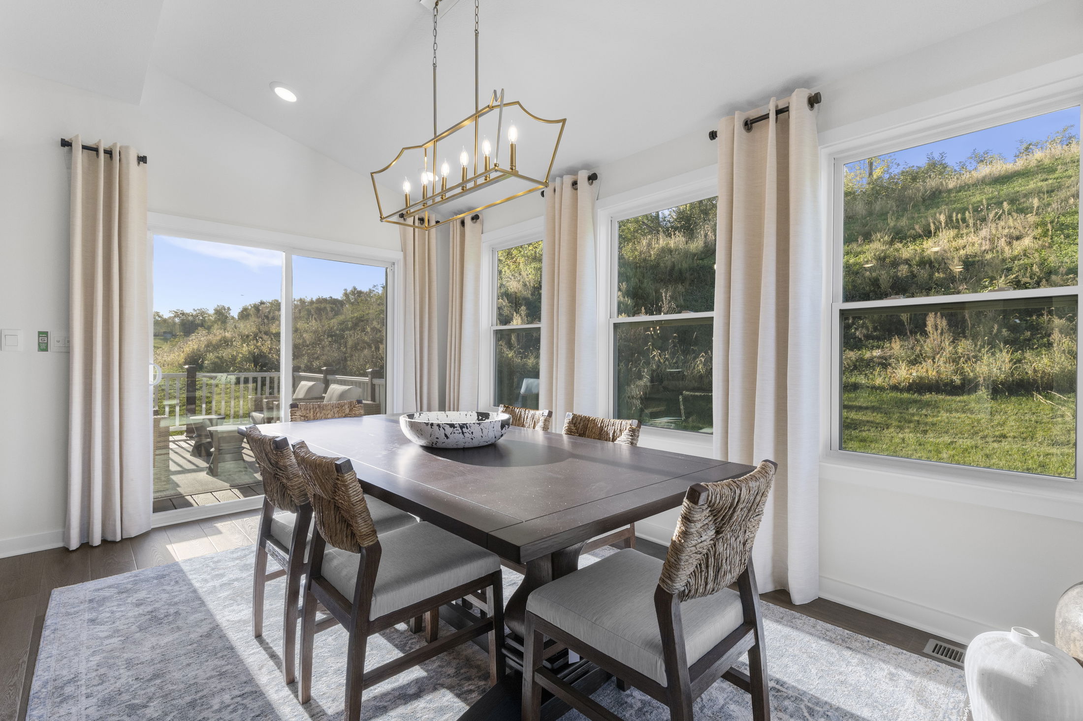 Modern dining room featuring a wooden table, upholstered chairs, large windows with scenic views, and elegant light fixtures.
