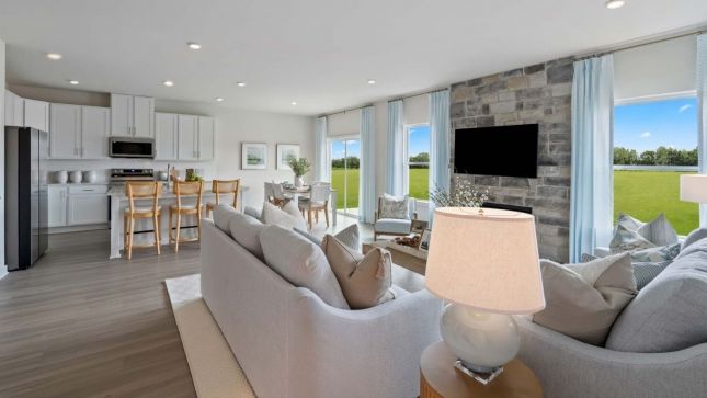 A modern living room with large windows, a cozy sofa, and a view of a grassy field.