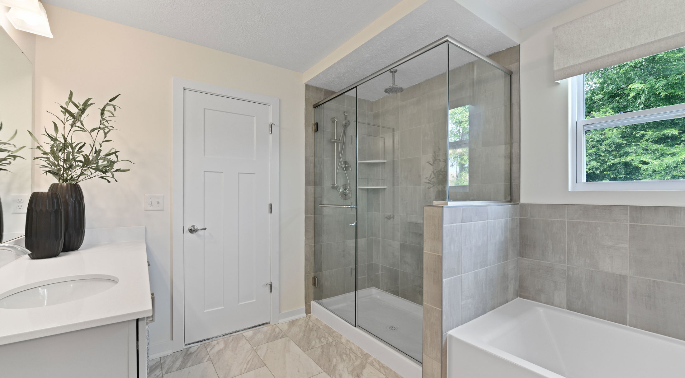 Modern bathroom featuring a glass-enclosed shower, white bathtub, and sleek vanity with decorative plants.