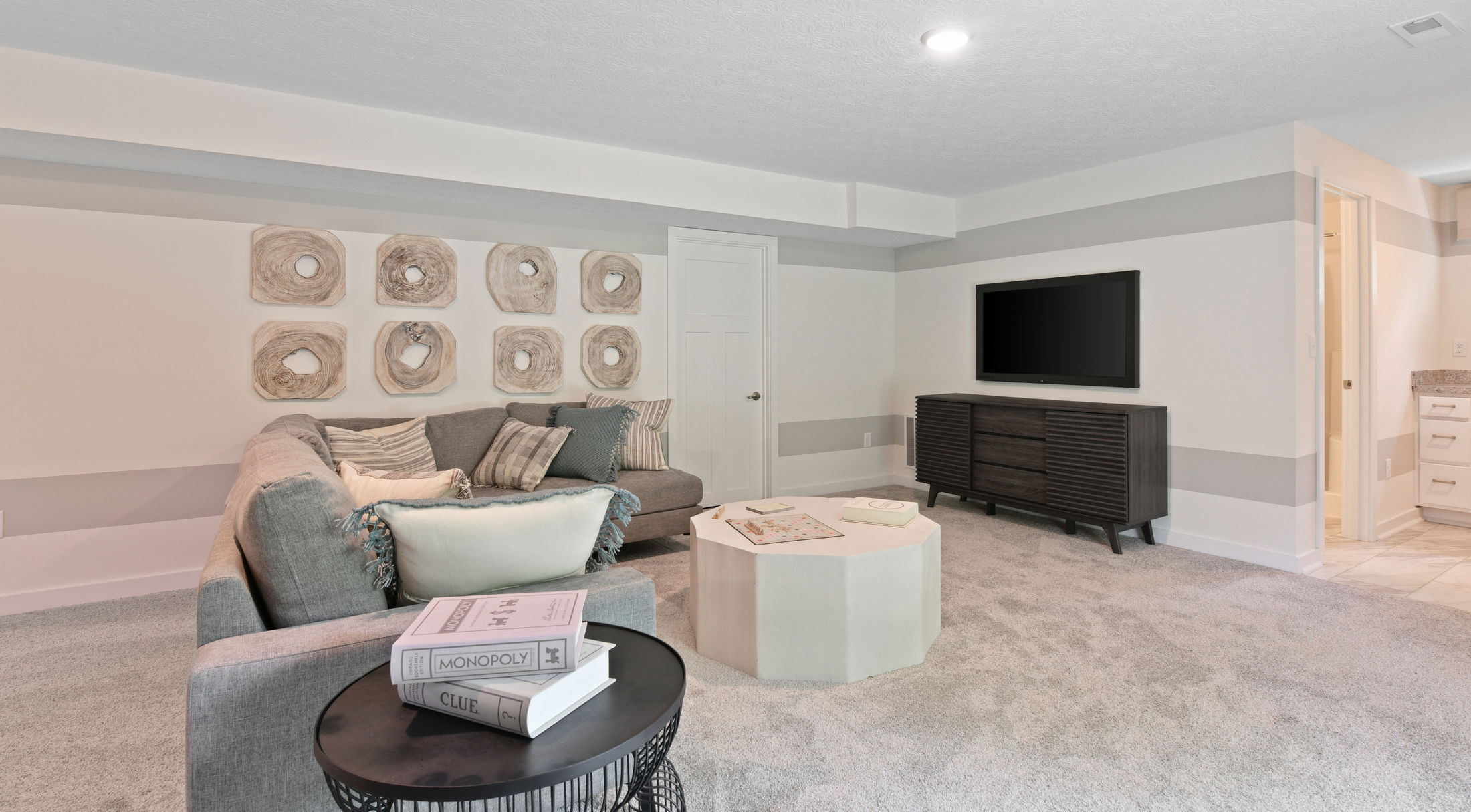Stylish basement living area with modern decor, featuring a large gray sectional sofa, wall-mounted TV, and a minimalist coffee table.