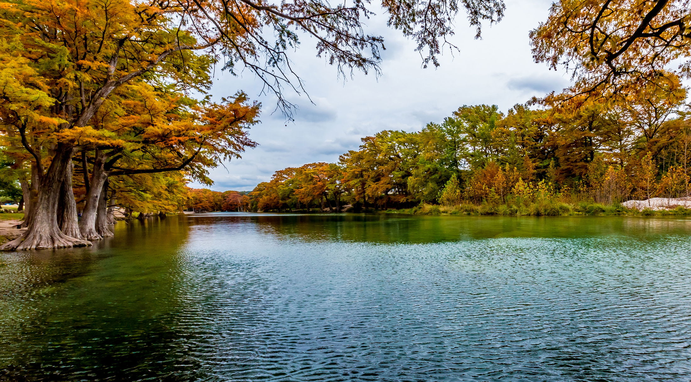 Serene river landscape with vibrant autumn trees lining the water\\\'s edge.