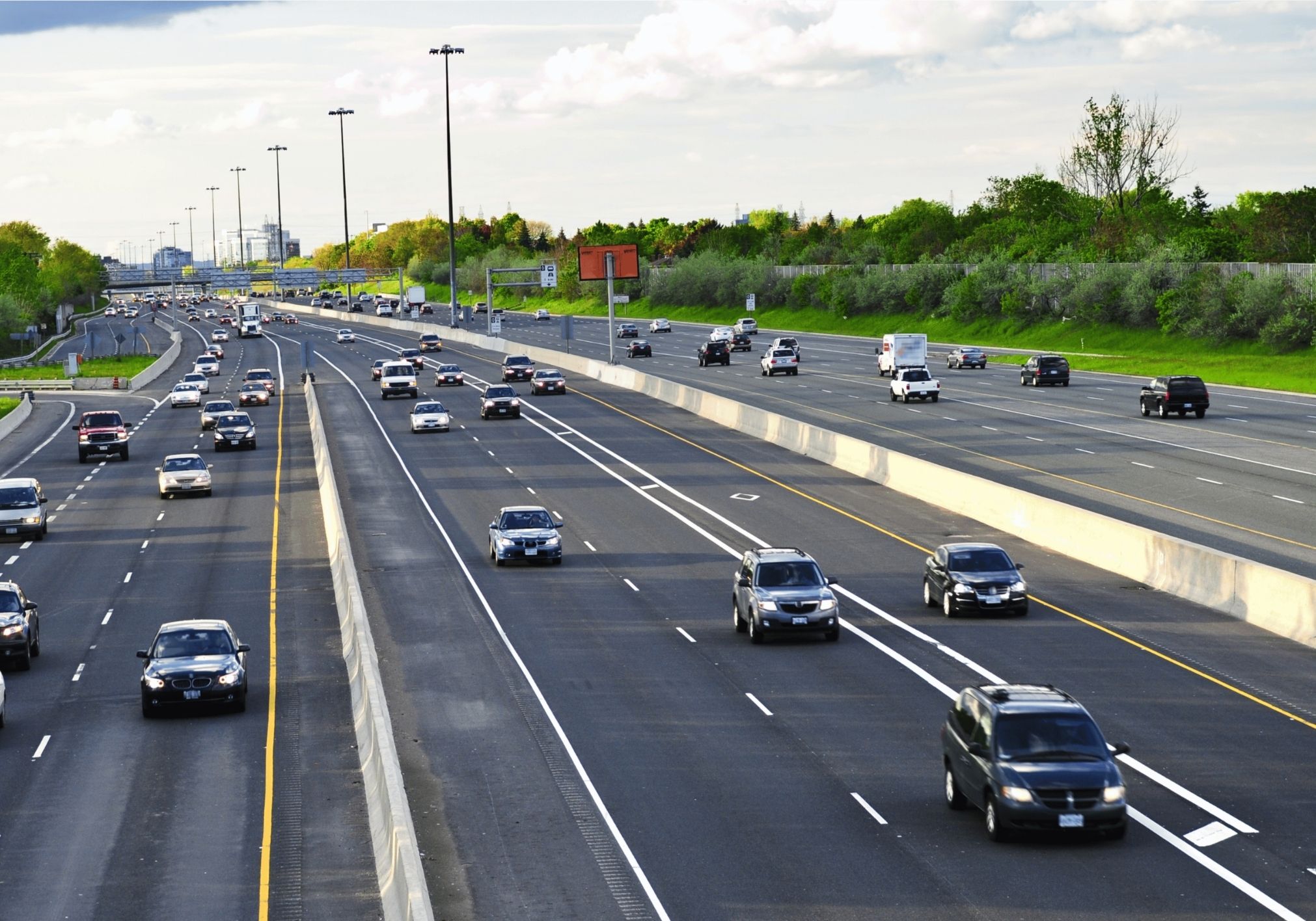 Busy highway with multiple lanes of vehicles and green trees lining the sides.