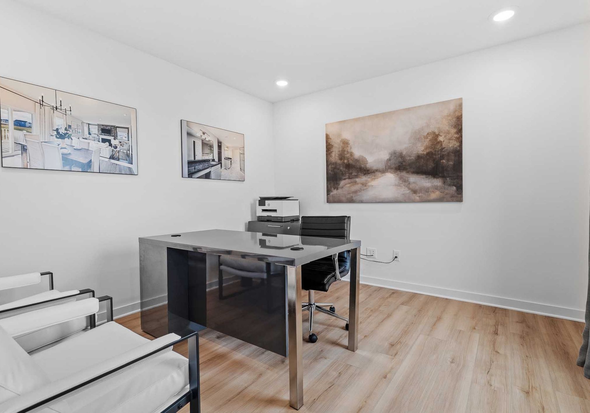 Modern office space featuring a glass desk, black chair, and two white armchairs, with artwork on the walls.
