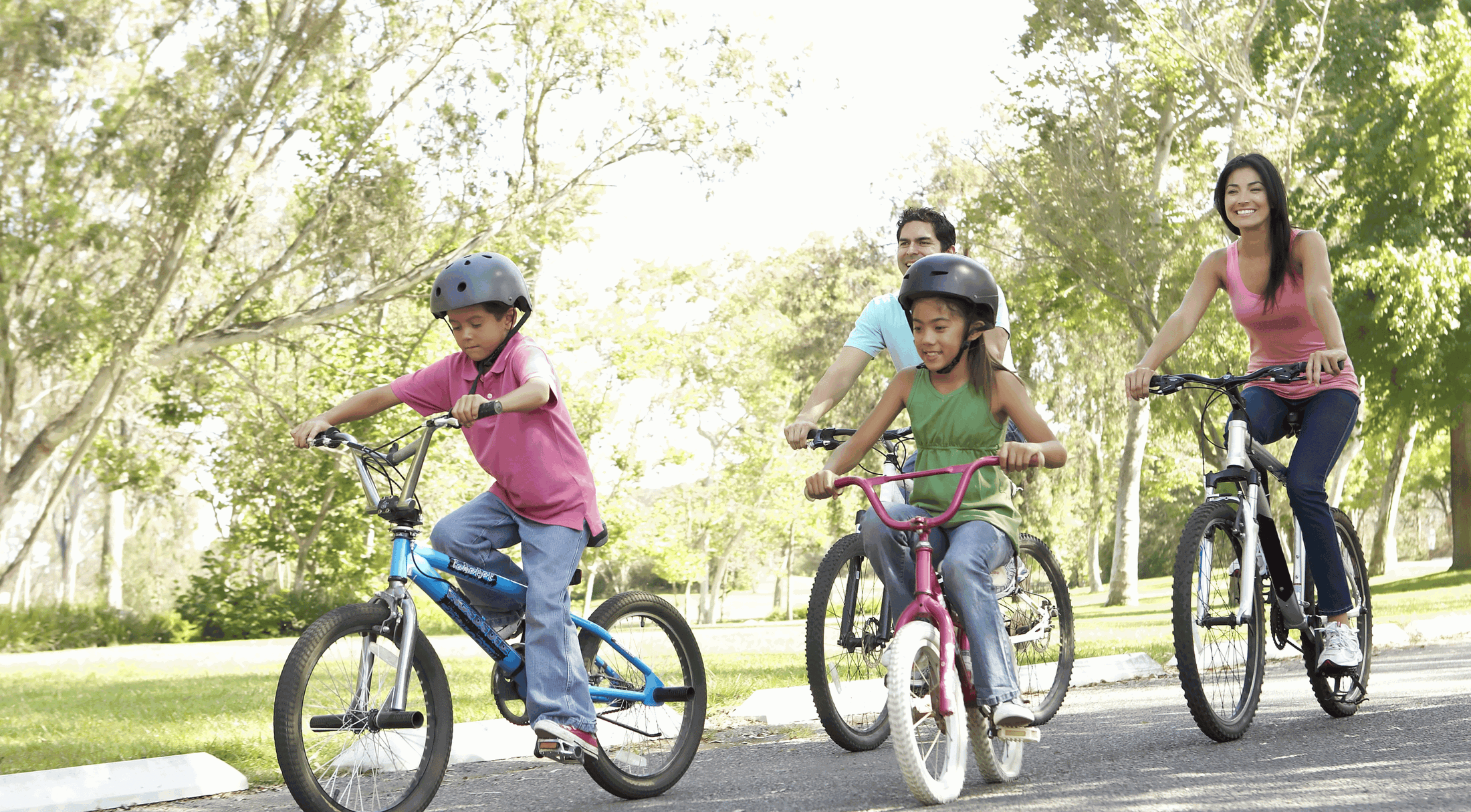 A family enjoying a bike ride together in a sunny park, wearing helmets for safety.