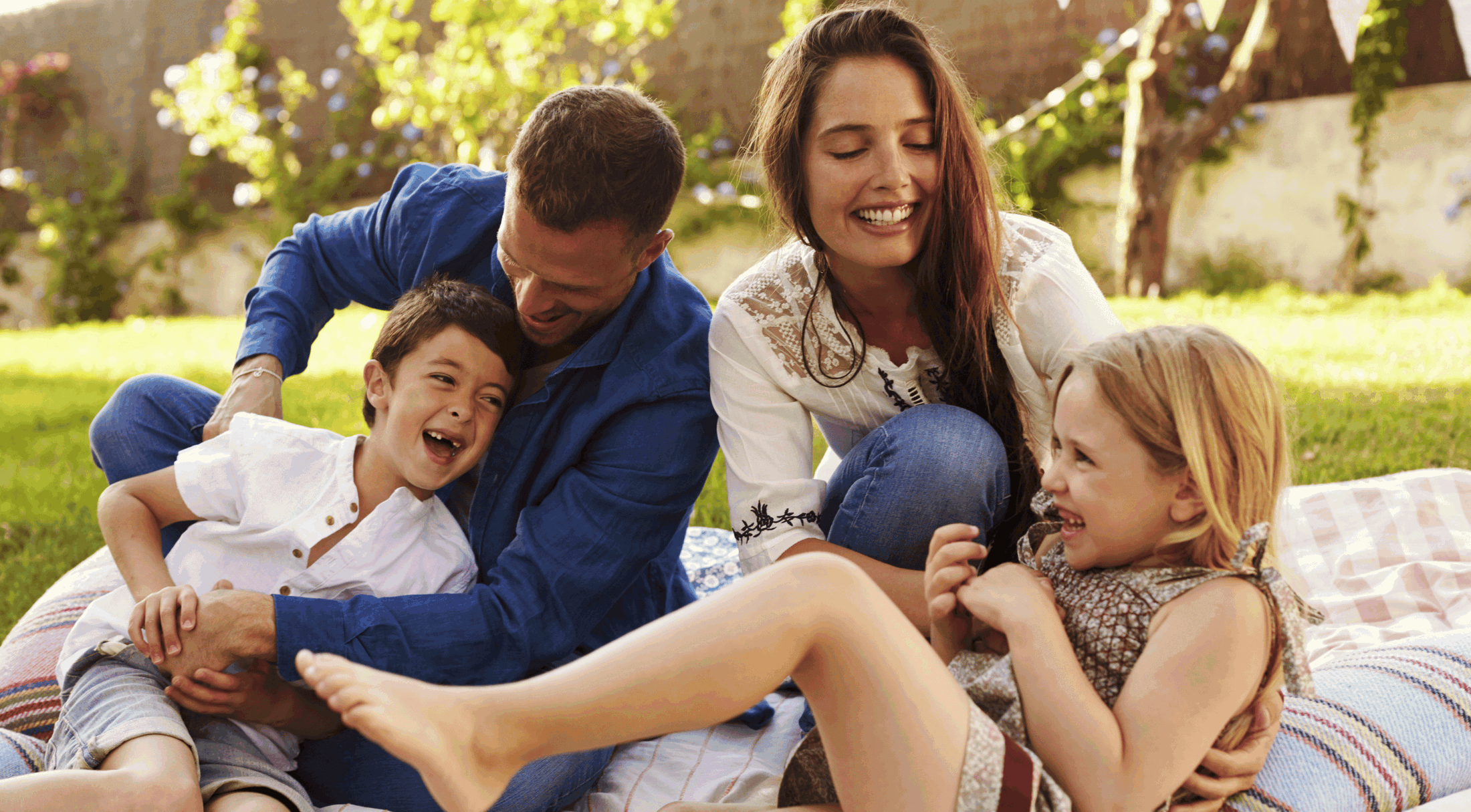 A happy family enjoys a picnic on a sunny day, laughing and playing together on a blanket in a lush garden.