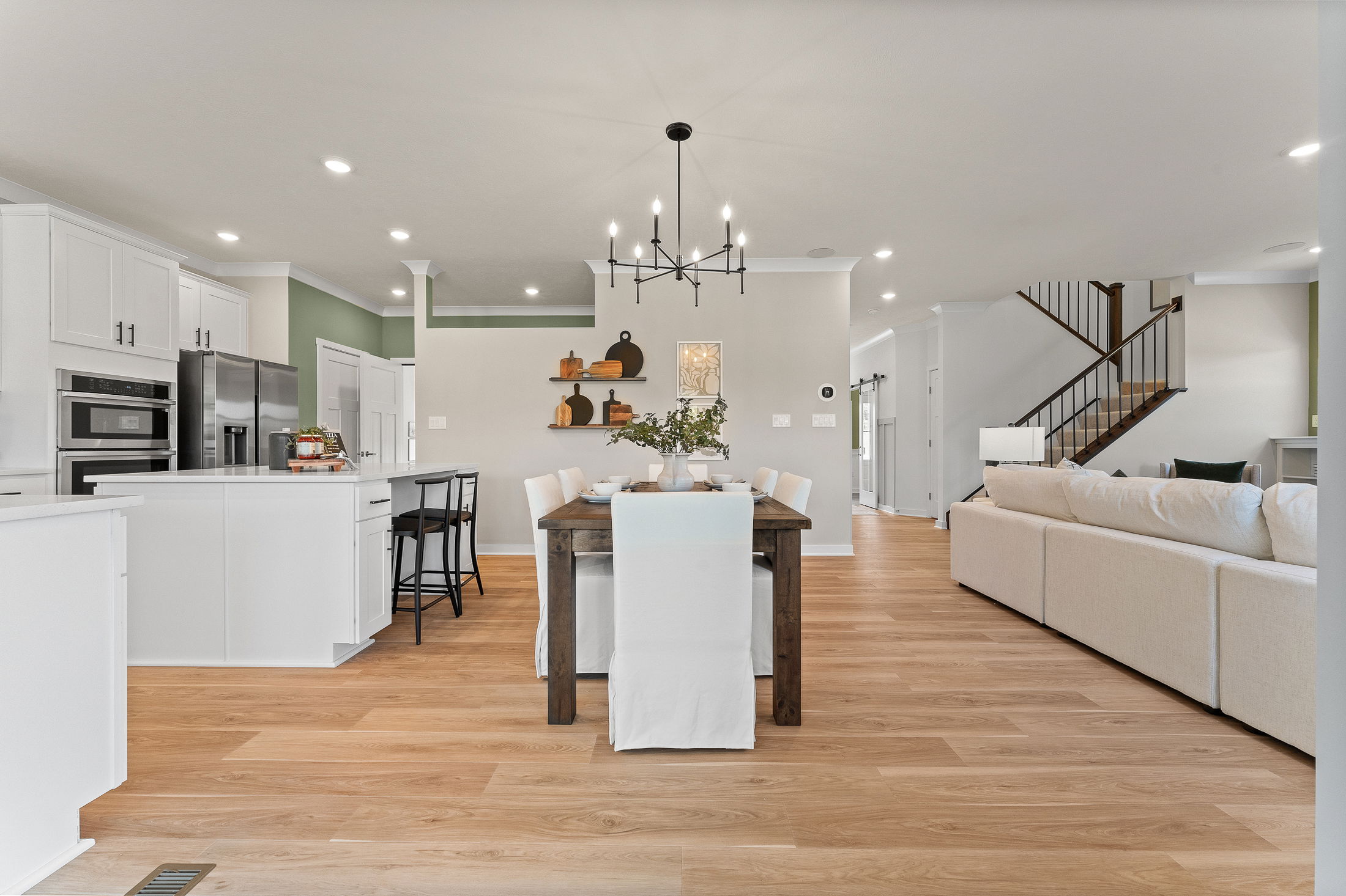 Modern open-concept living area featuring a stylish dining room table, contemporary kitchen with island, and cozy seating area with natural wood flooring.