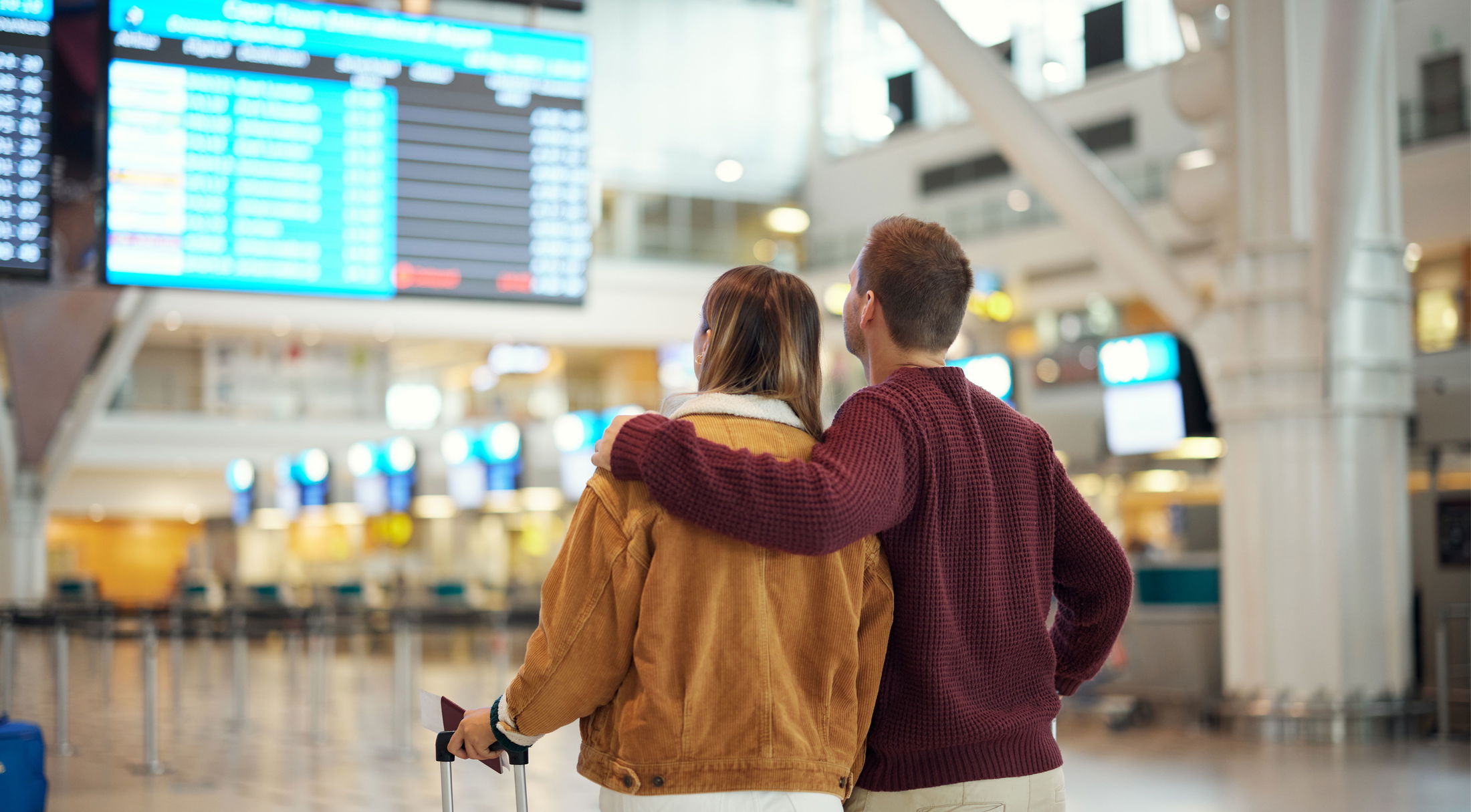 A couple at an airport terminal looks at the flight departure board with anticipation.