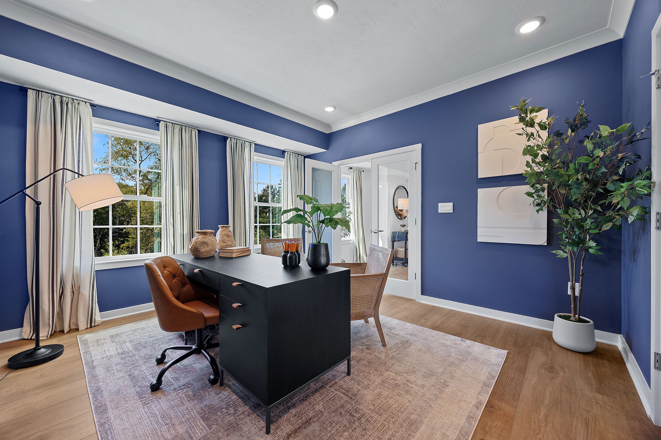 Elegant home office with blue walls, natural light, modern furnishings, and stylish decor.