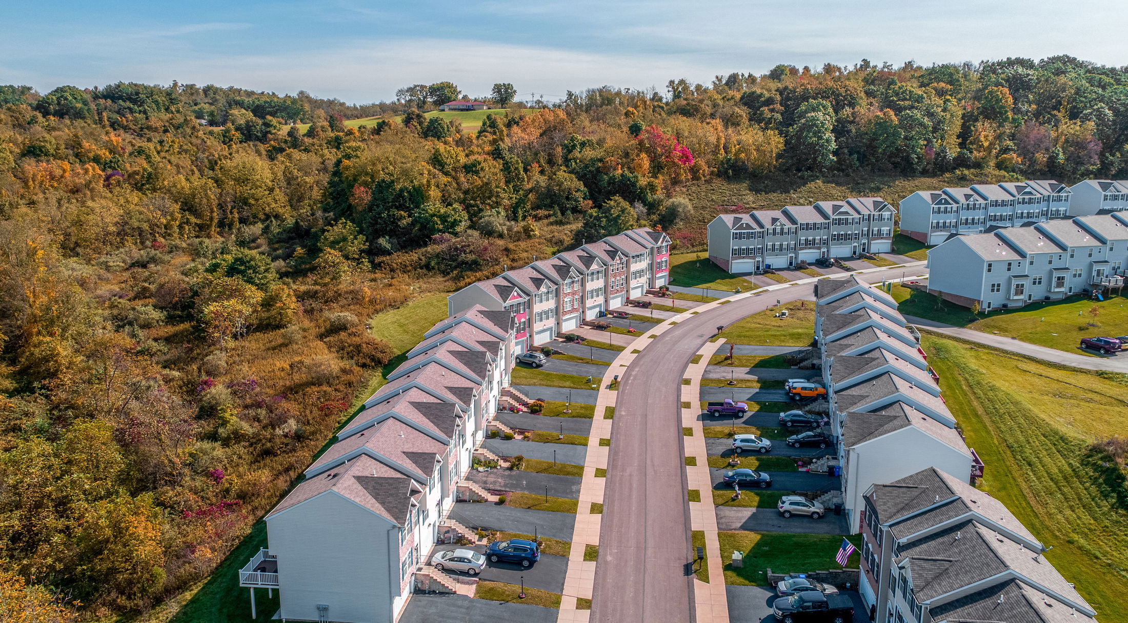 Aerial view of a suburban neighborhood with rows of townhouses and lush autumn foliage in the background.