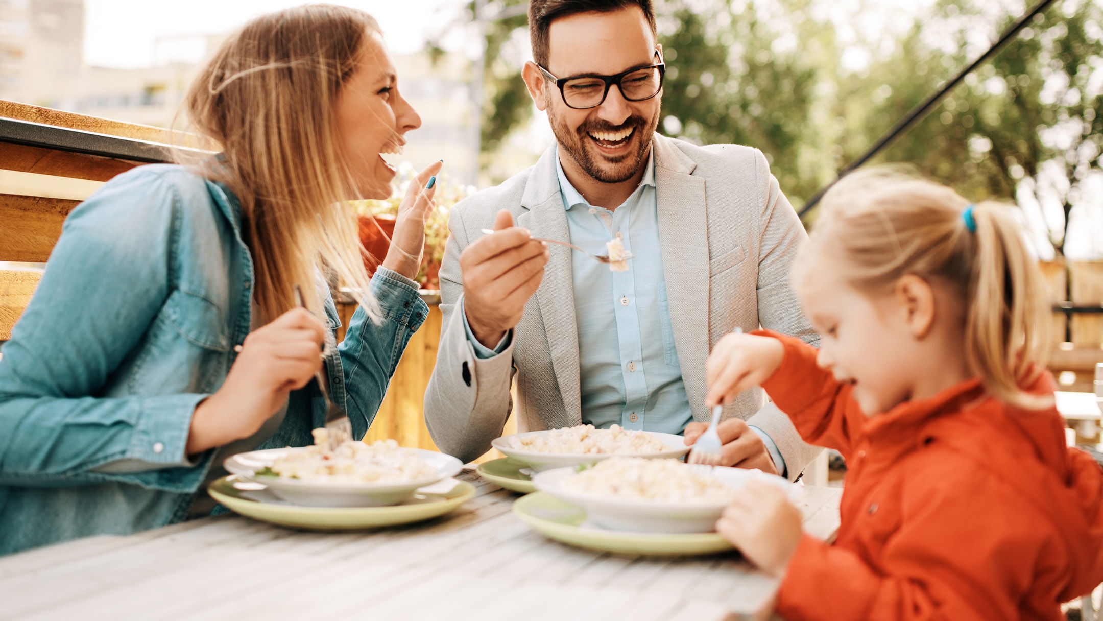 A family enjoying a meal together outdoors, with smiling faces and plates of food on the table.