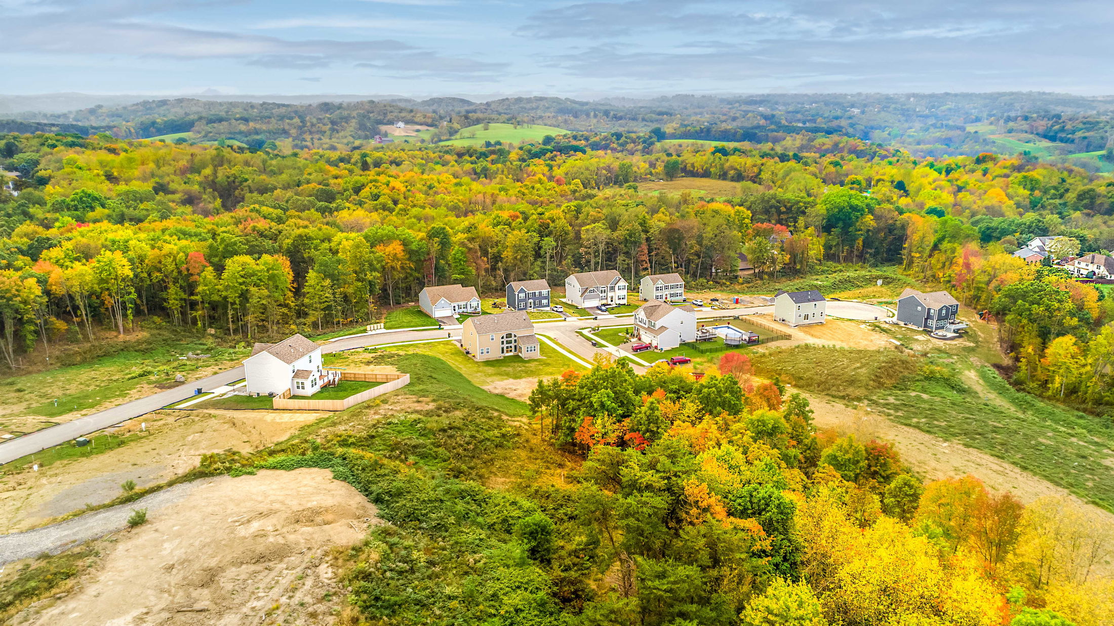 Aerial view of a rural residential neighborhood surrounded by vibrant autumn foliage and rolling hills.