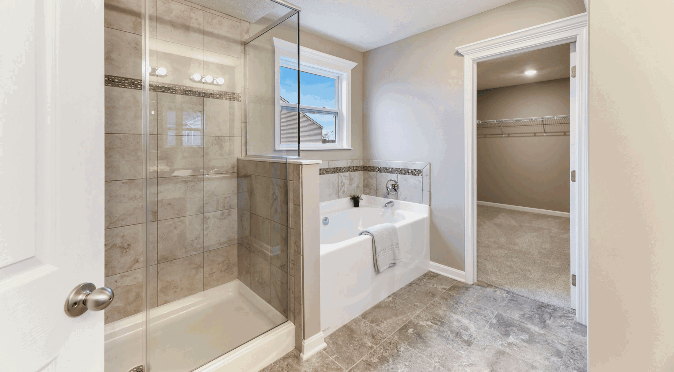 Luxurious bathroom with a glass shower, tiled bathtub, and open walk-in closet.