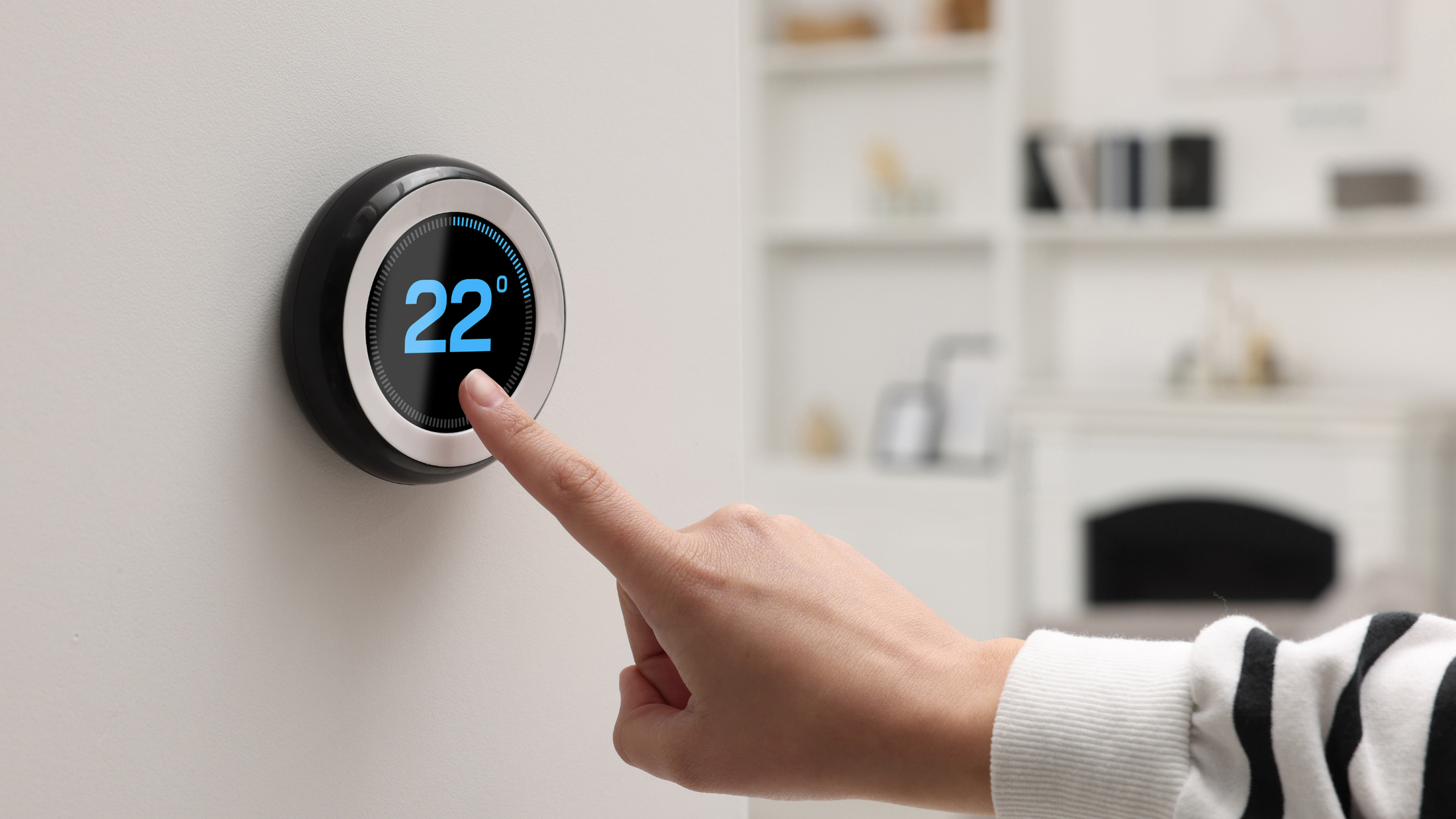 Person adjusting smart thermostat to 22 degrees Celsius in a modern home setting.
