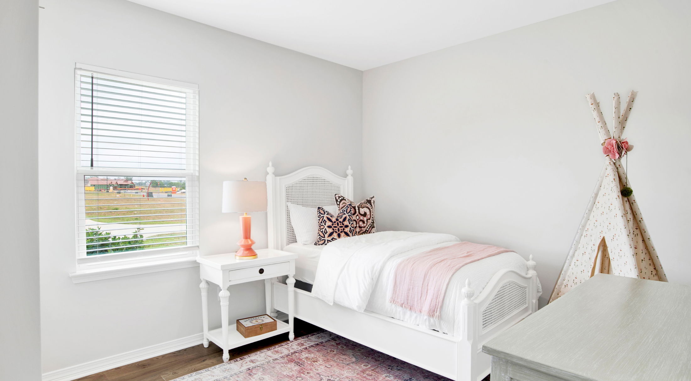 Charming minimalistic bedroom with a single white bed, colorful pillows, bedside table, and decorative teepee tent.