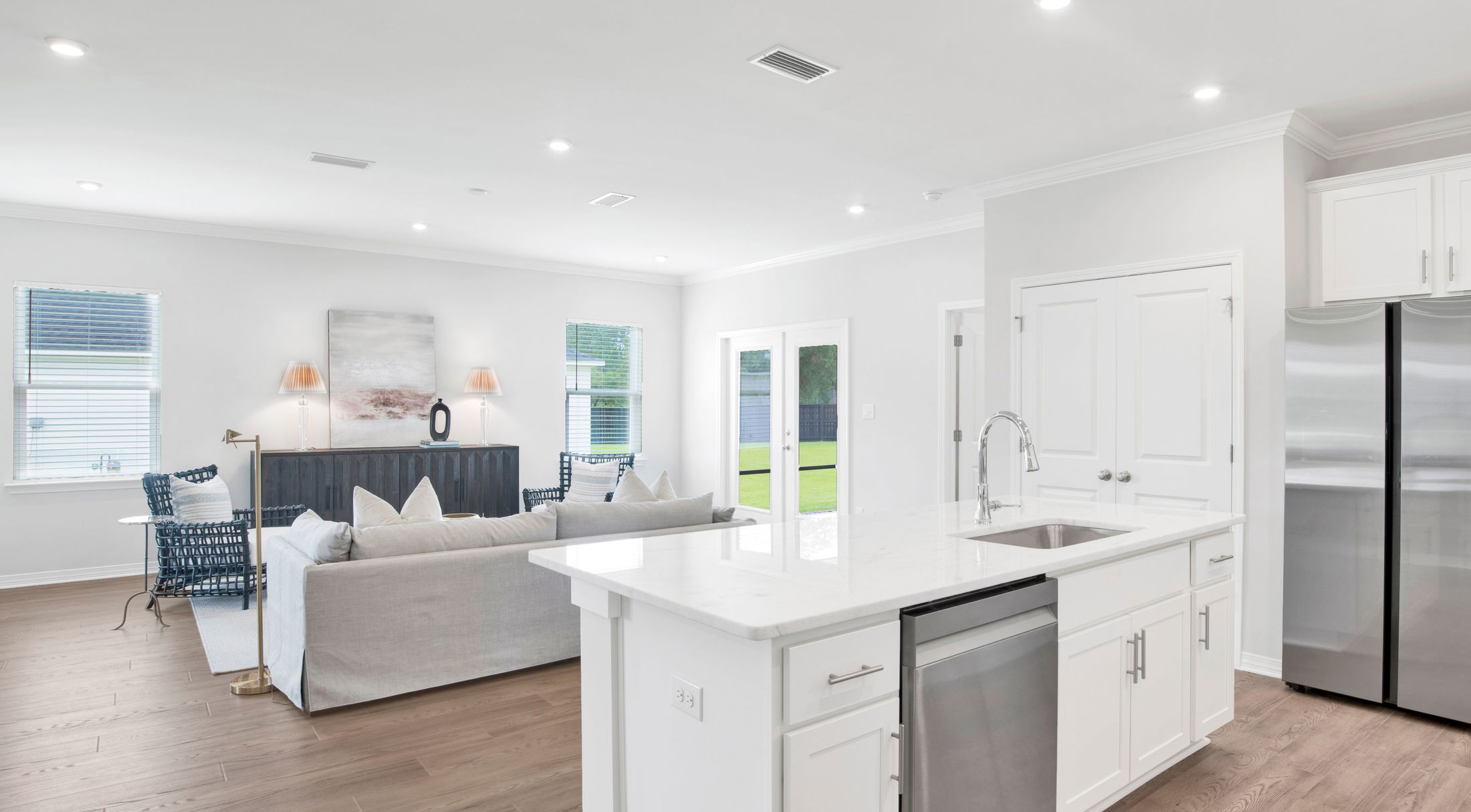 Modern open-concept kitchen and living room with white cabinets, stainless steel appliances, and hardwood flooring.