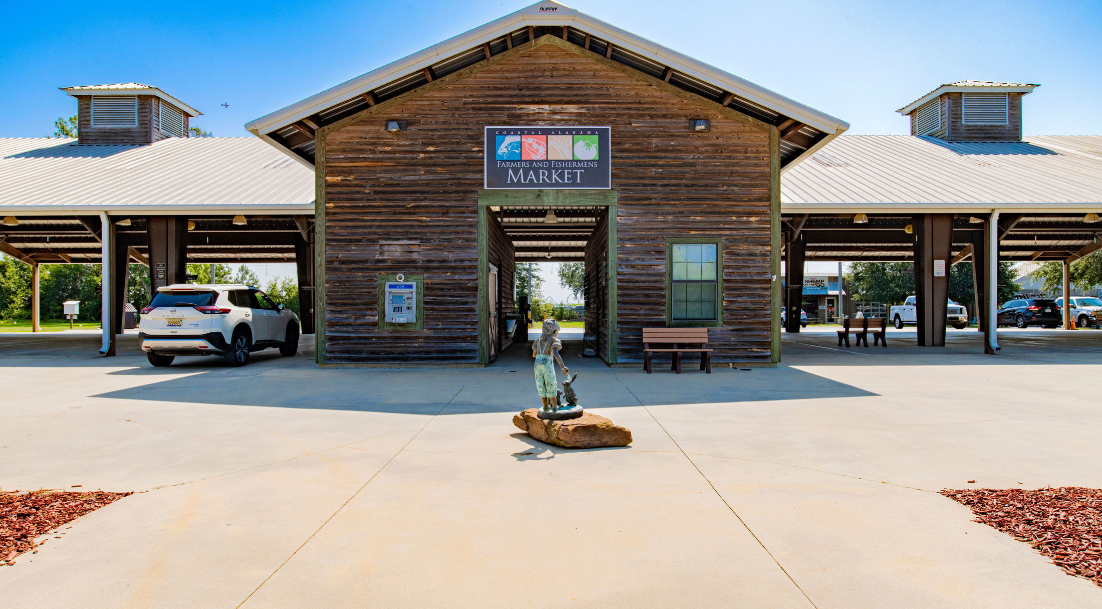 Rustic wooden exterior of Coastal Alabama Farmers and Fishermens Market on a sunny day with cars parked nearby.