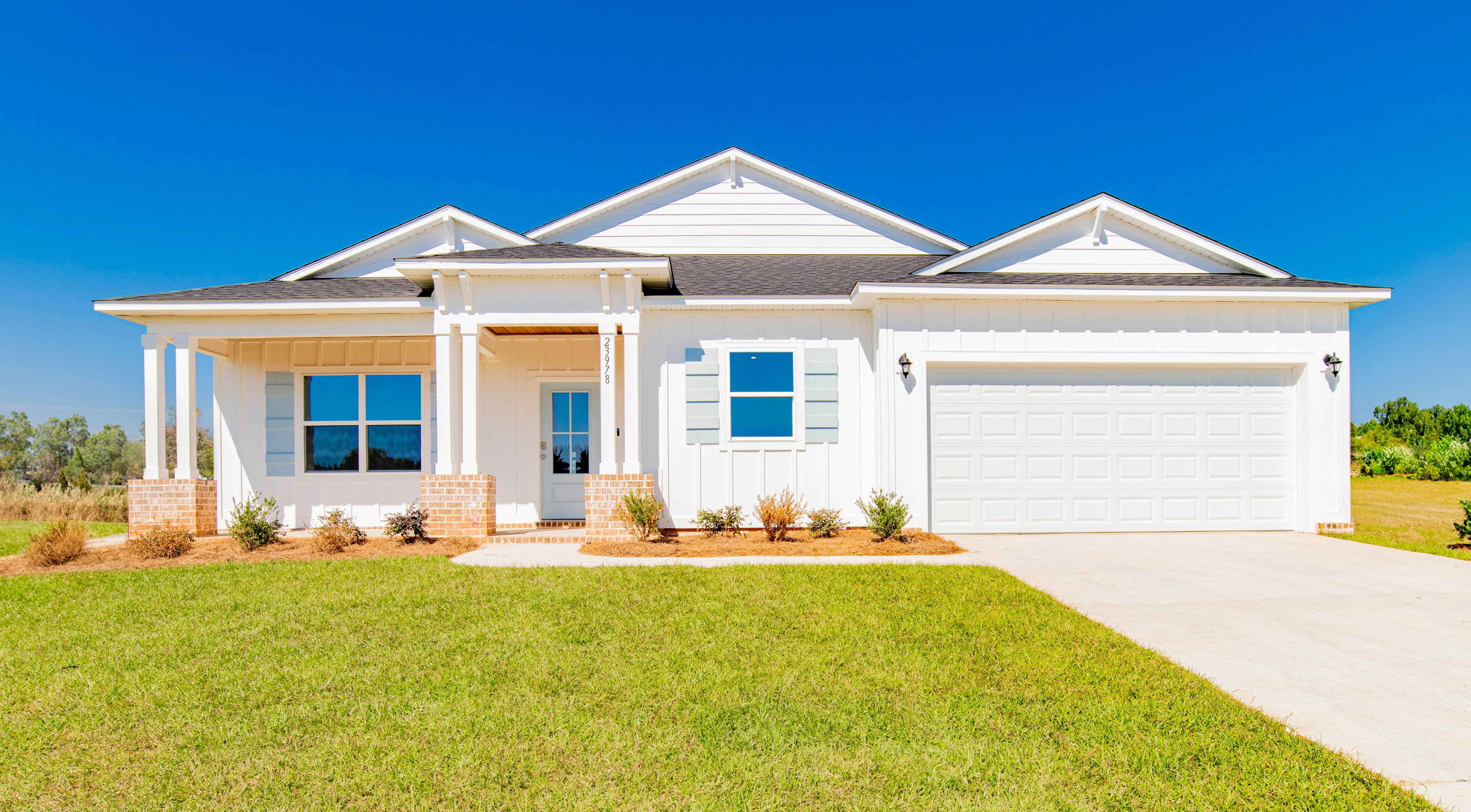 Modern single-story white house with a two-car garage and a manicured lawn under a clear blue sky.