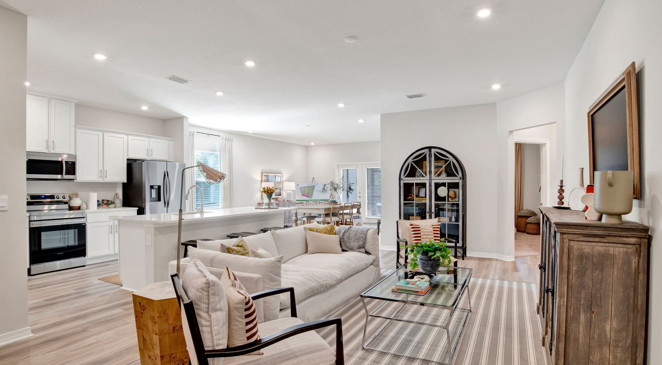 Modern open-concept living room and kitchen with white cabinets, stylish decor, and natural light.
