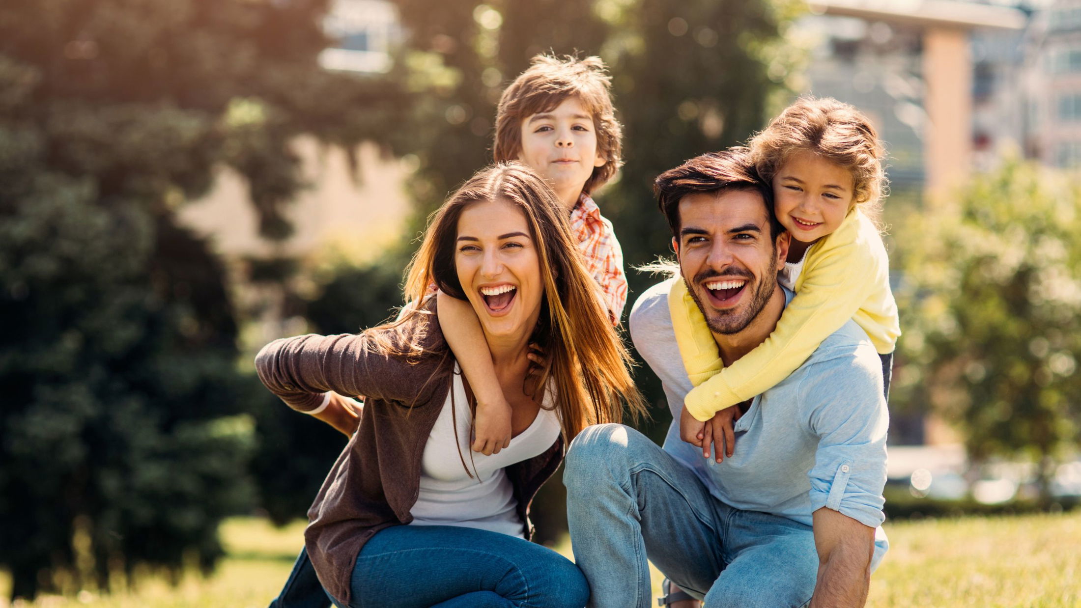 Happy family enjoying a sunny day outdoors, with parents giving piggyback rides to their children.