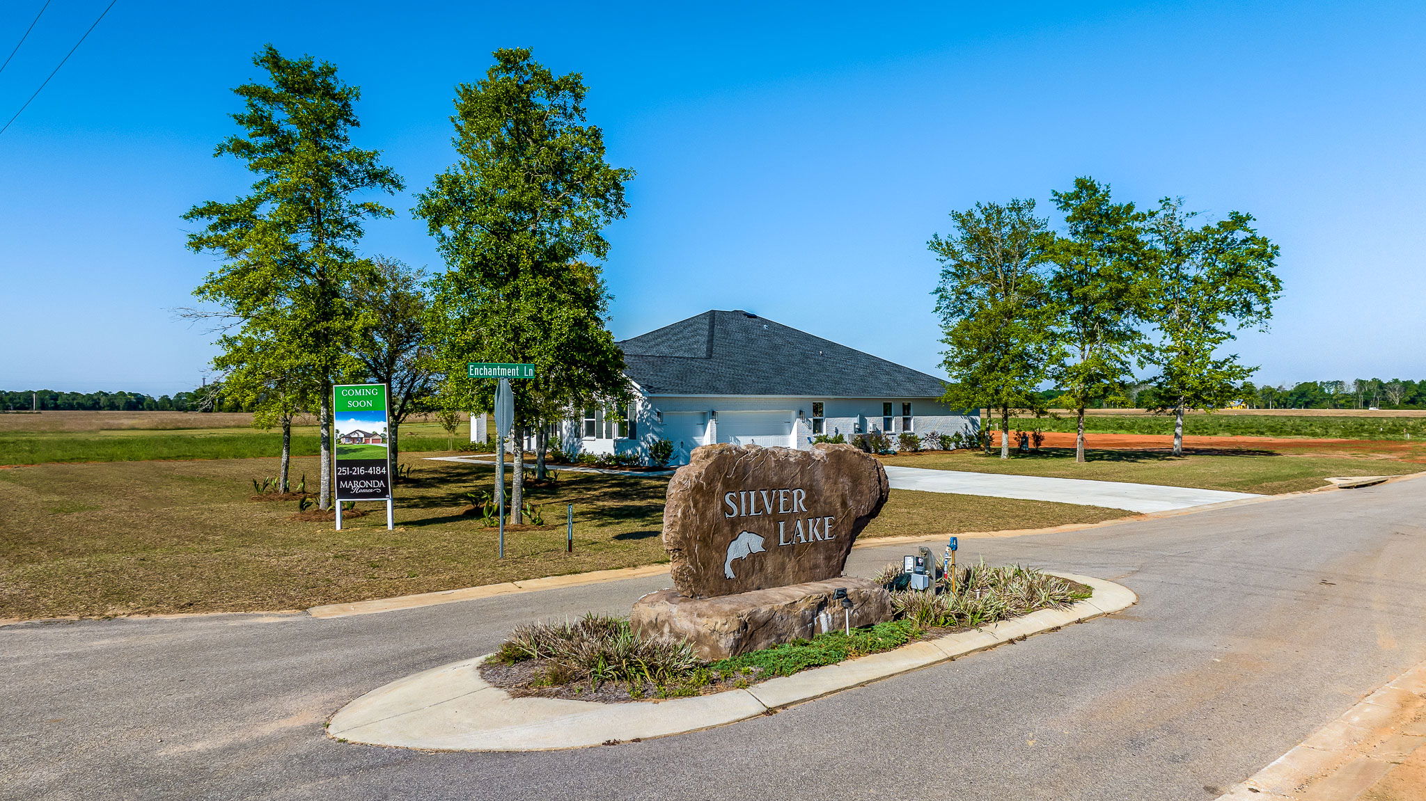Entrance to Silver Lake residential development with a large rock sign and a house in the background under a clear blue sky.