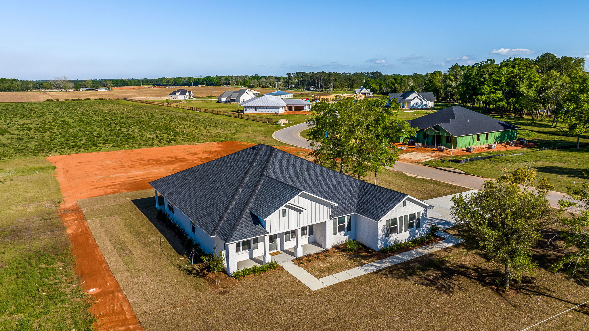 Aerial view of a modern white house with a black roof in a newly developed rural neighborhood.