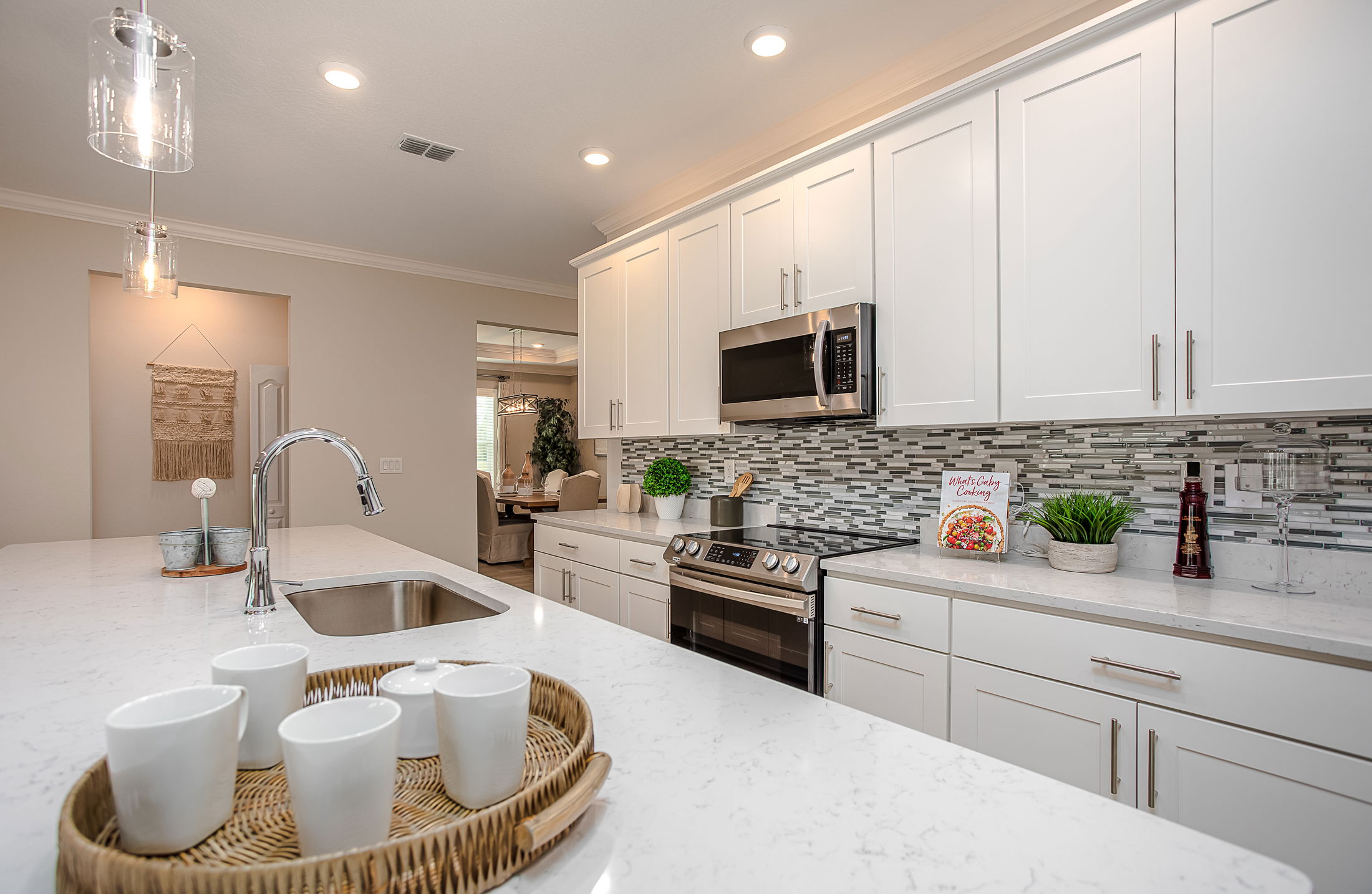 Modern white kitchen with stainless steel appliances, a mosaic tile backsplash, and a marble countertop featuring a decorative tray with cups.