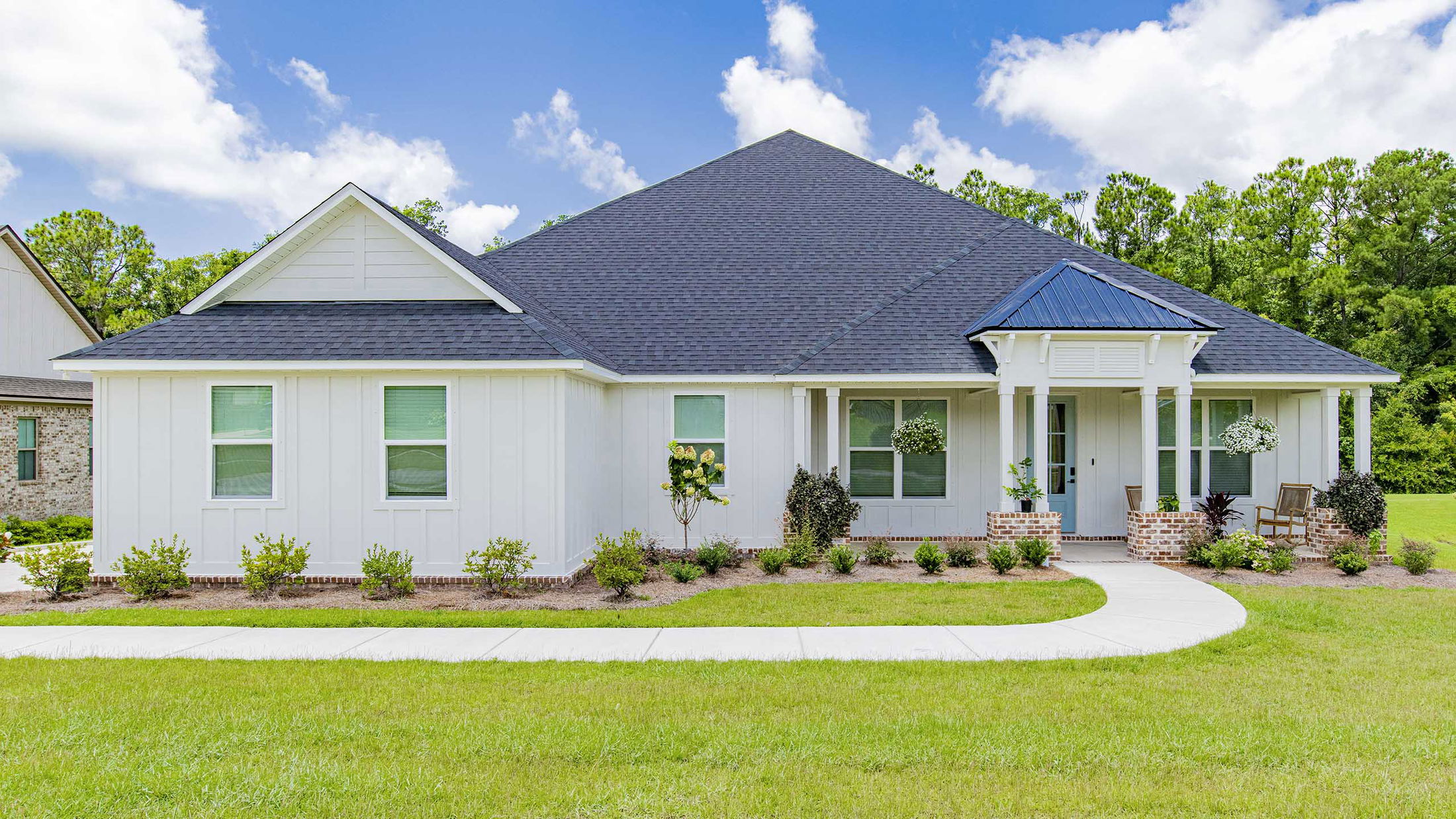 Beautiful single-story modern white house with a dark roof, landscaped garden, and inviting front porch.