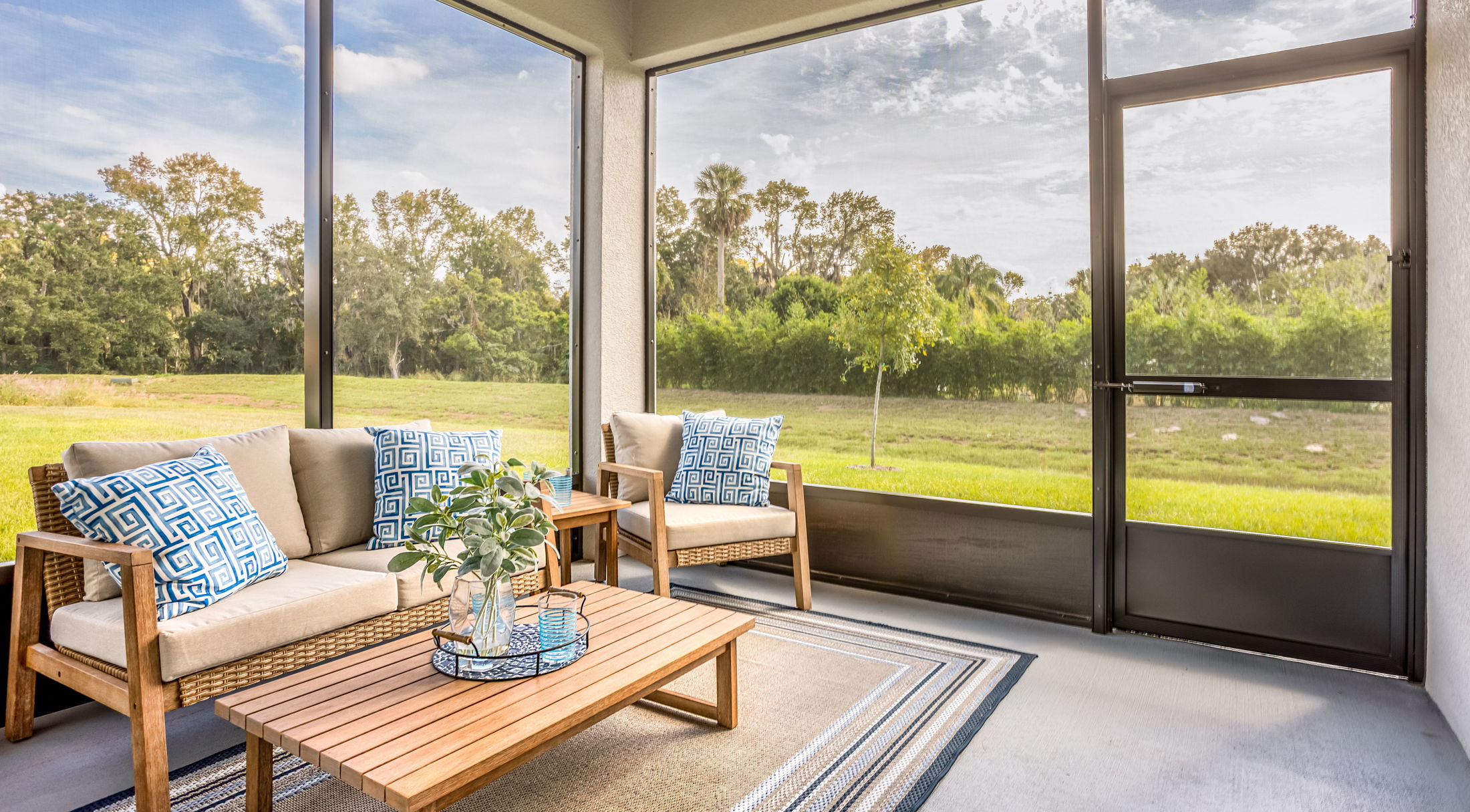 Screened-in patio with wooden furniture and cushions overlooking a lush green backyard.