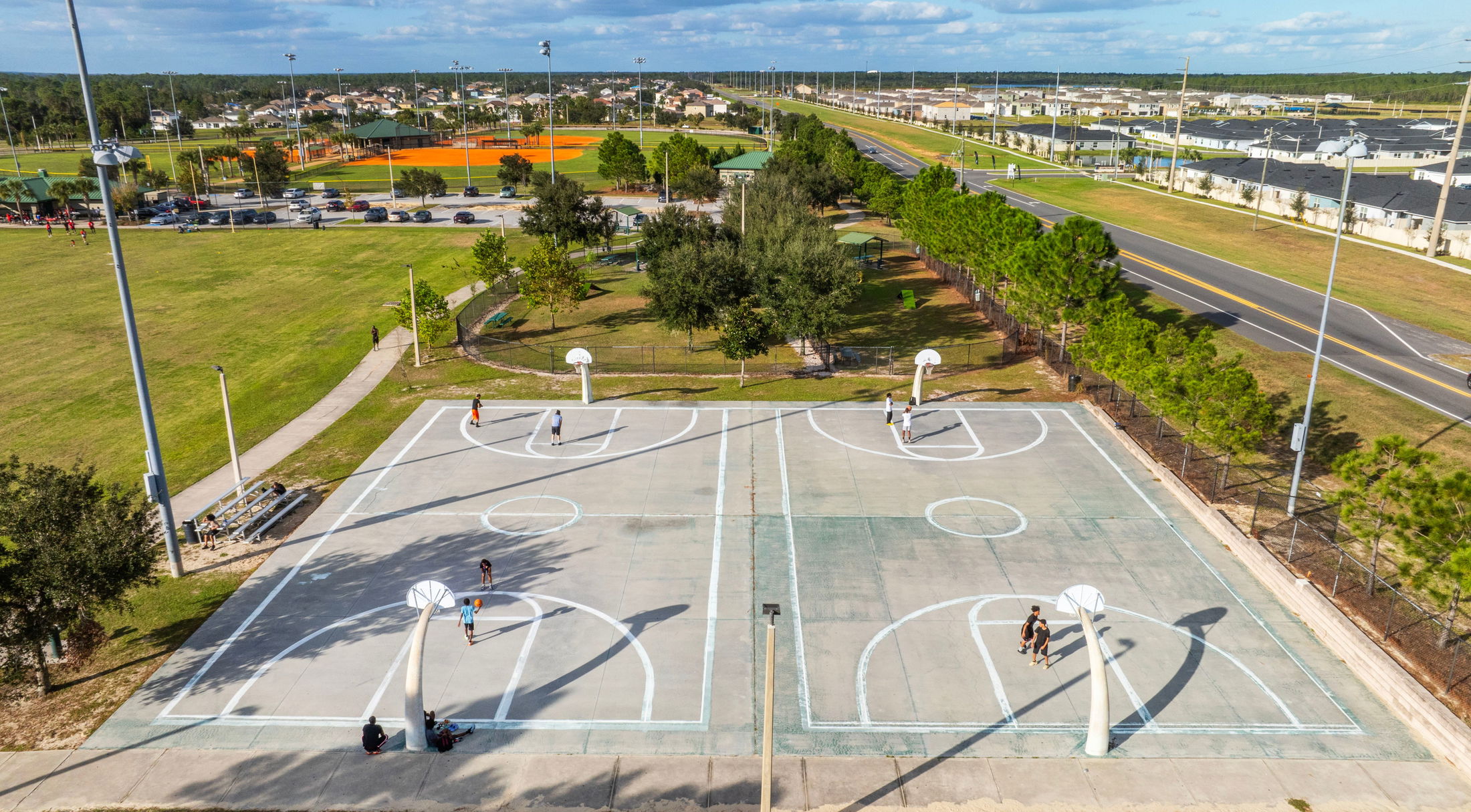 Aerial view of outdoor basketball courts in a park setting with people playing basketball on a sunny day.