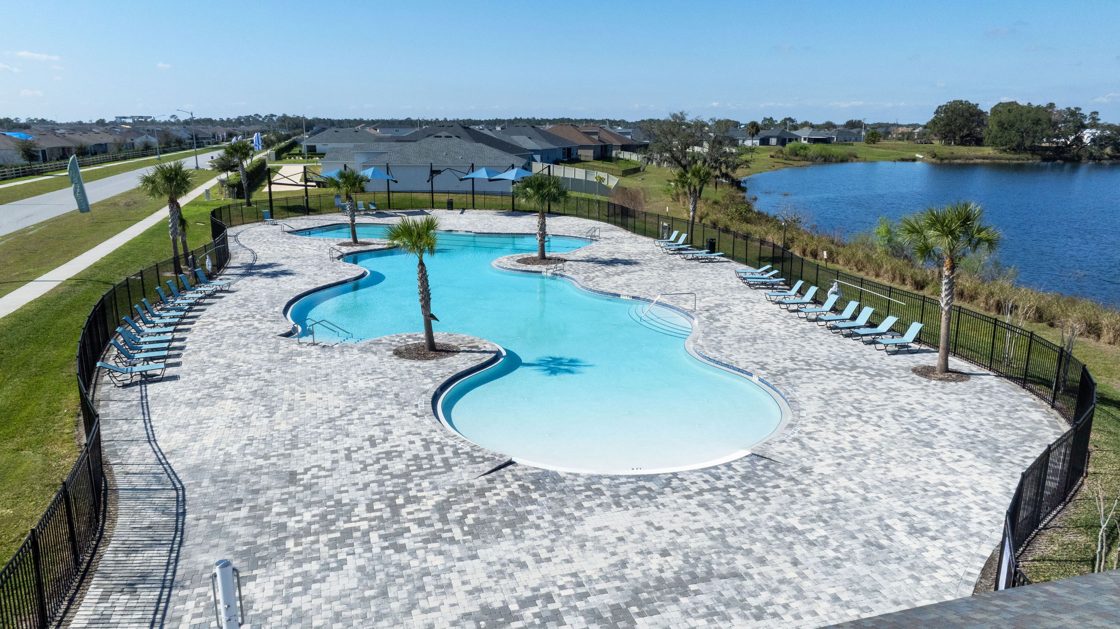 Aerial view of a resort-style swimming pool with lounge chairs, palm trees, and a lake in the background.