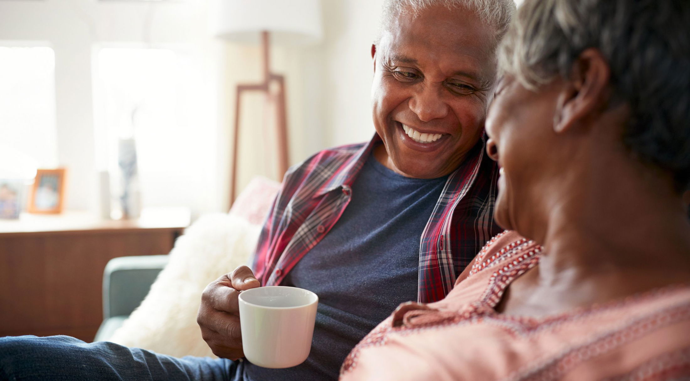 Smiling older couple enjoying a cozy moment at home, with the man holding a coffee mug.