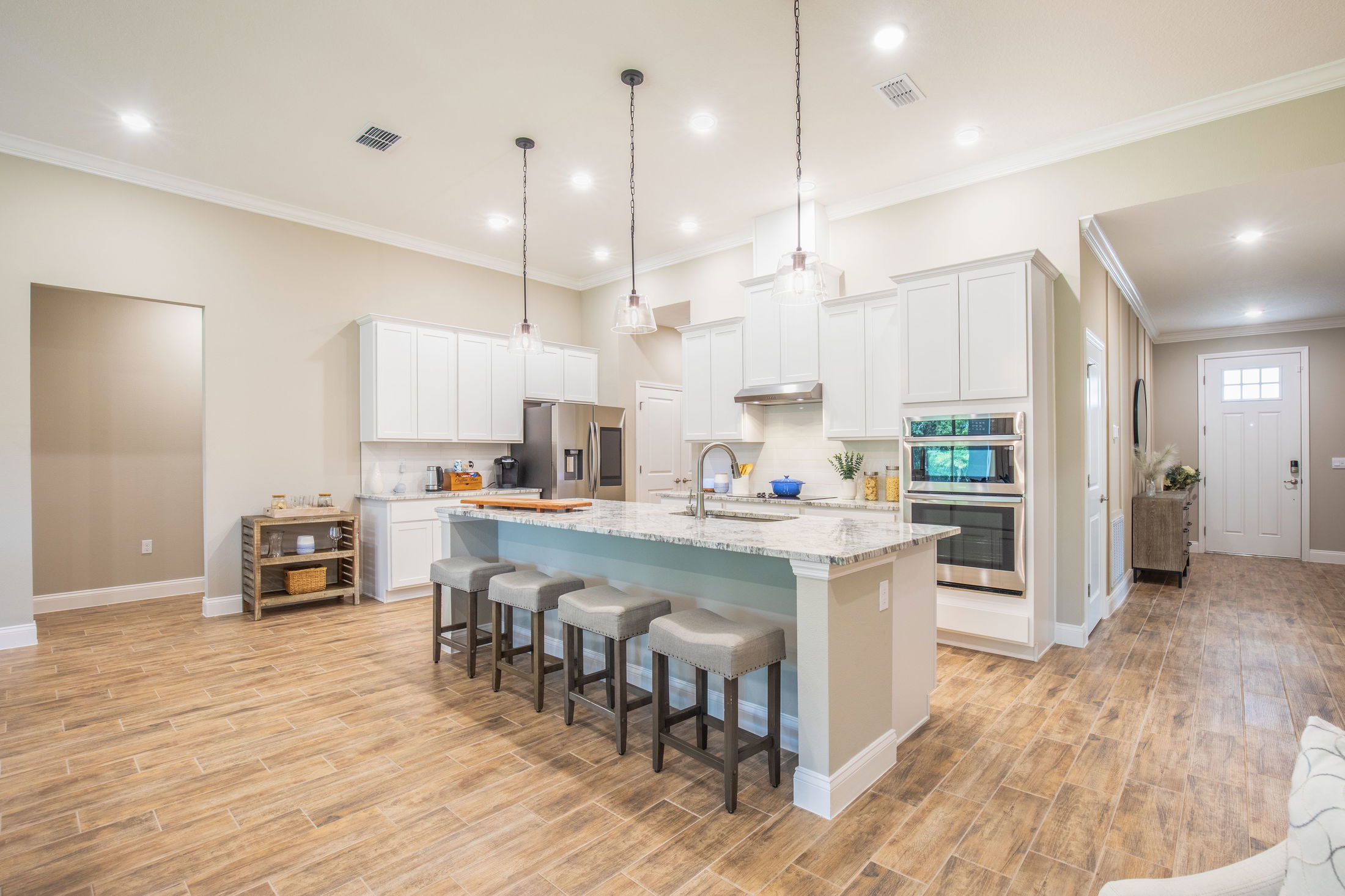 Modern kitchen interior with a large granite island, pendant lighting, white cabinets, and wood-style flooring.