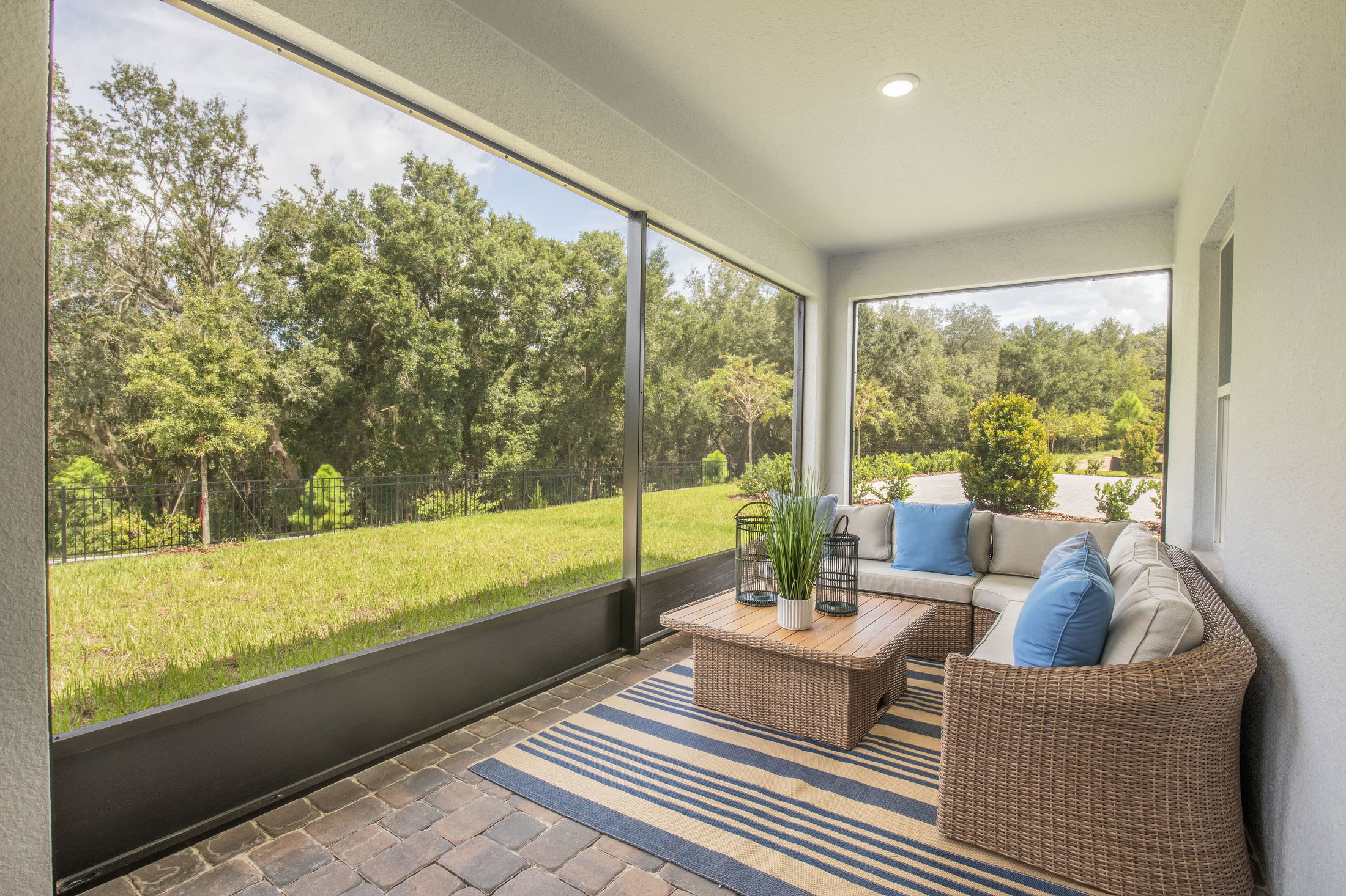 Spacious screened-in patio with wicker furniture, cushions, and a view of a lush green lawn and trees.