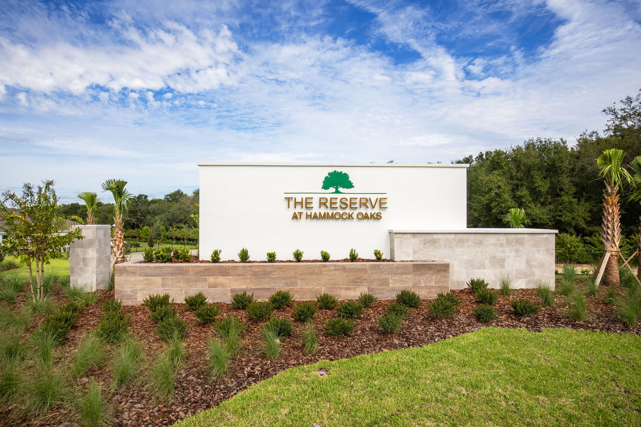 Entrance sign for The Reserve at Hammock Oaks, surrounded by landscaped greenery under a clear blue sky.