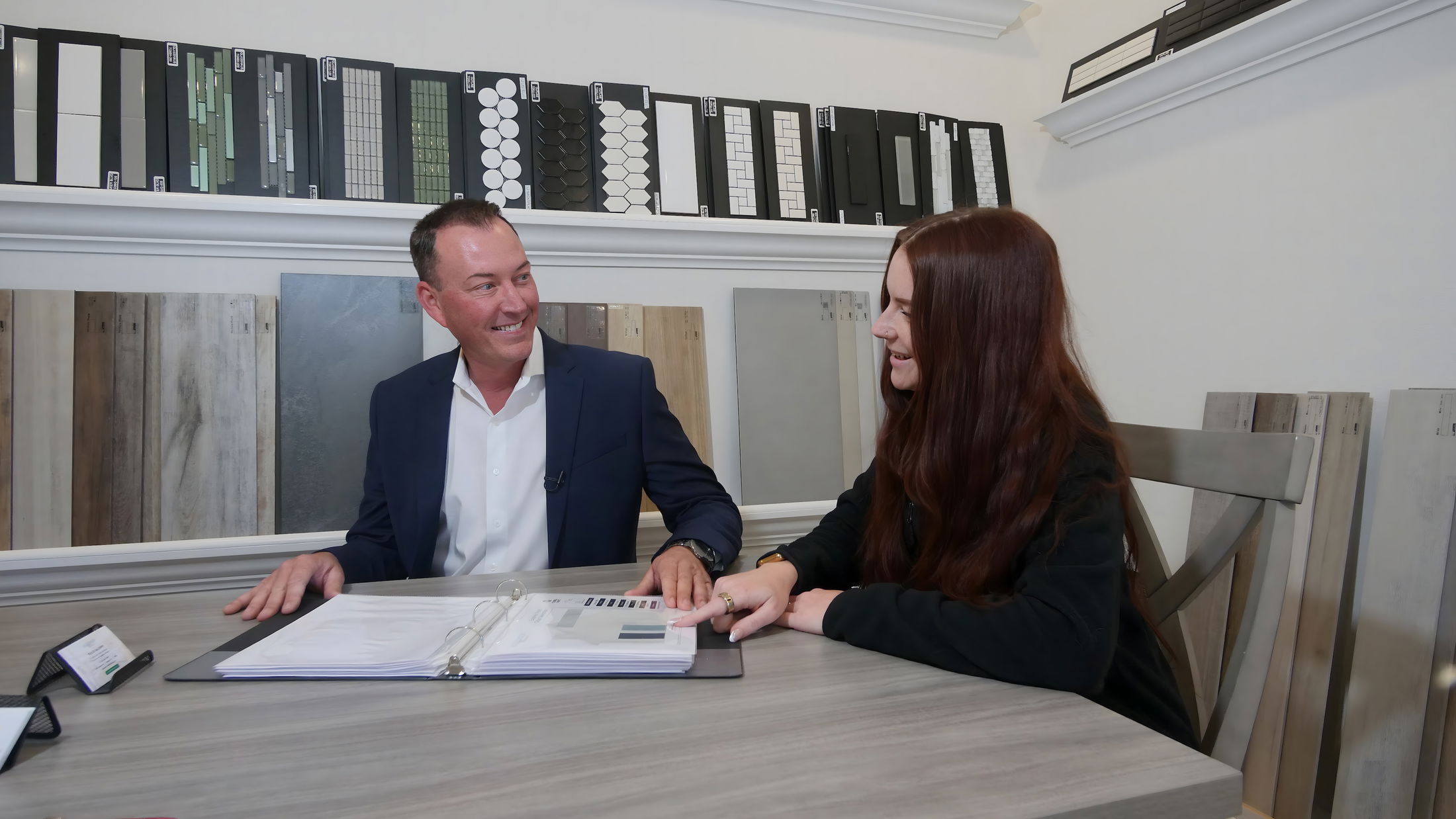 A professional consultation between a man and a woman discussing design choices with material samples on the table in a modern interior design studio.