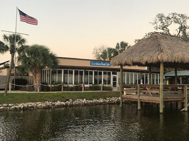 Scenic view of Leesburg Boat Club with palm trees and a thatched-roof structure by the water.