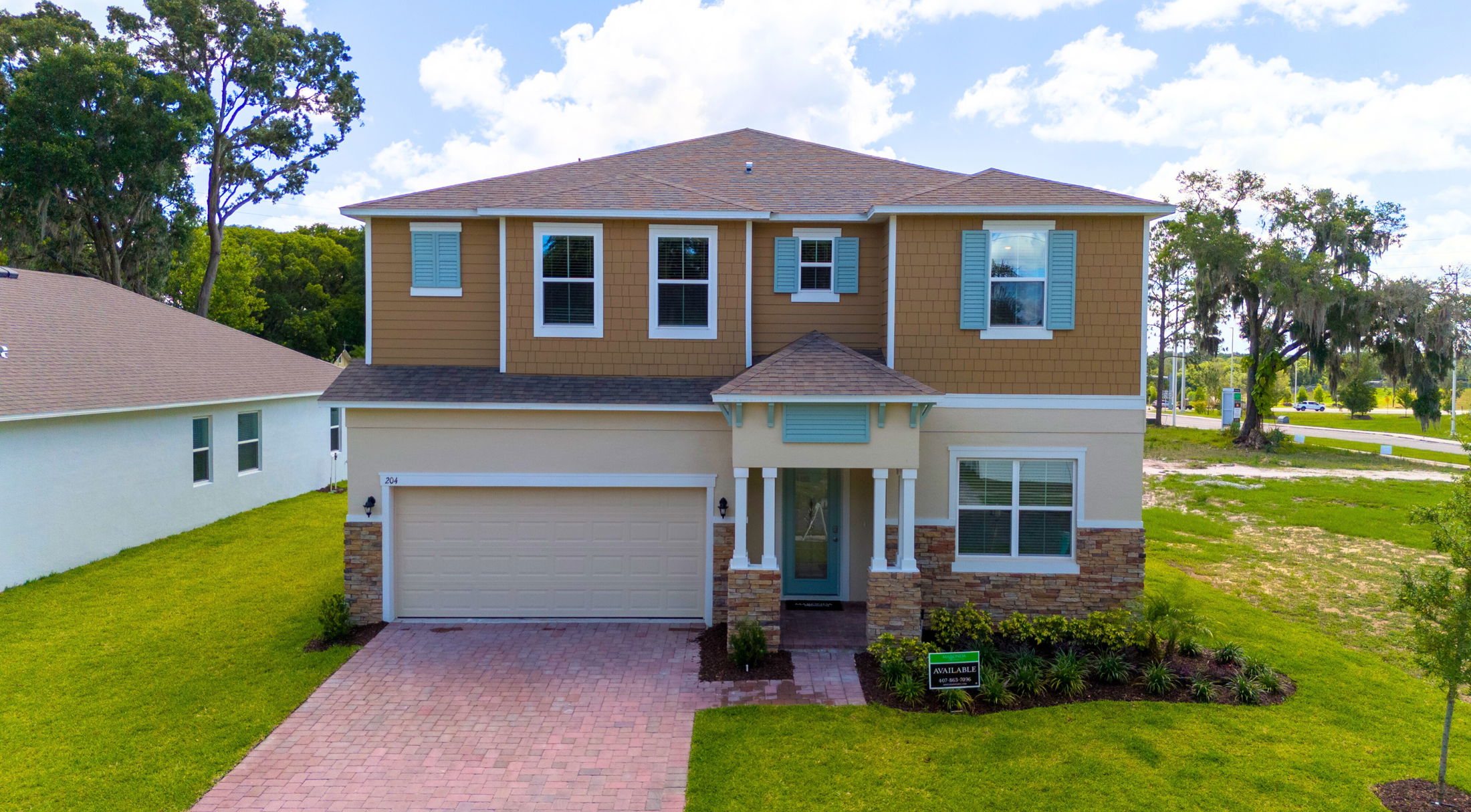 Modern two-story suburban home with a brick driveway and landscaped front yard under a clear blue sky.