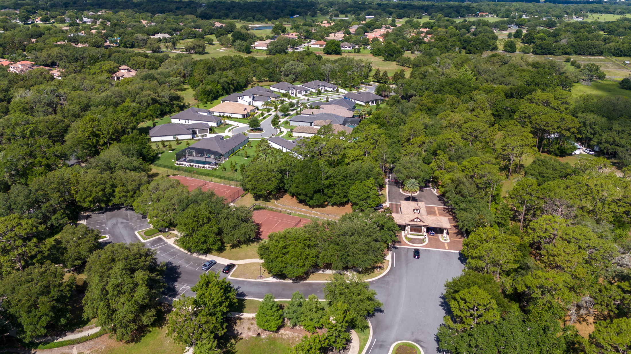 Aerial view of a suburban neighborhood with modern homes, surrounded by lush greenery and a tennis court.