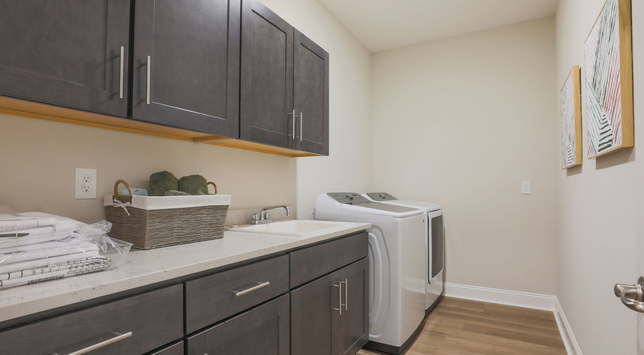 Modern laundry room with dark cabinets, countertop space, a sink, and a white washer and dryer set.