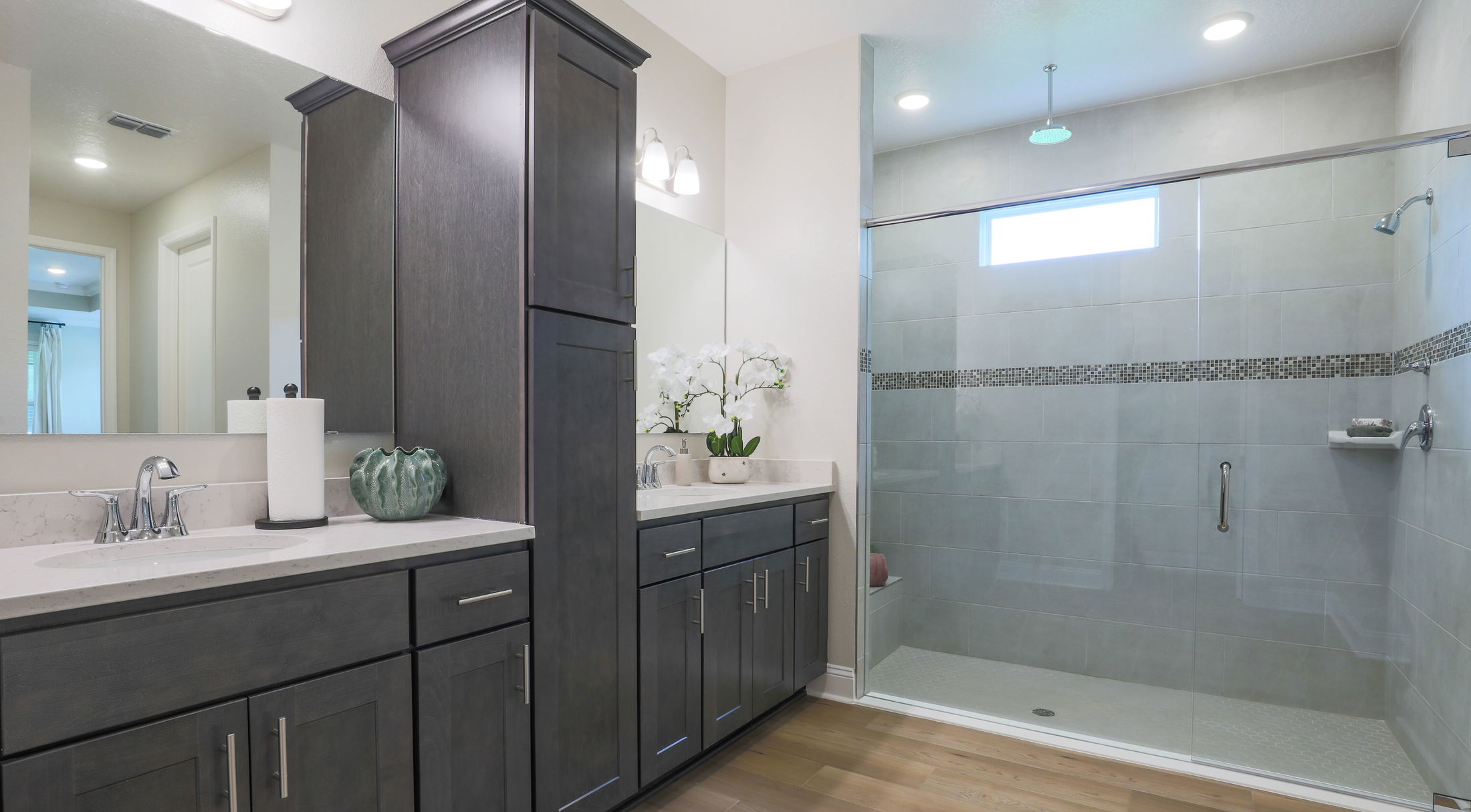 Modern bathroom with dark wood cabinets, a marble countertop, and a spacious walk-in shower featuring light gray tiles and decorative mosaic accents.
