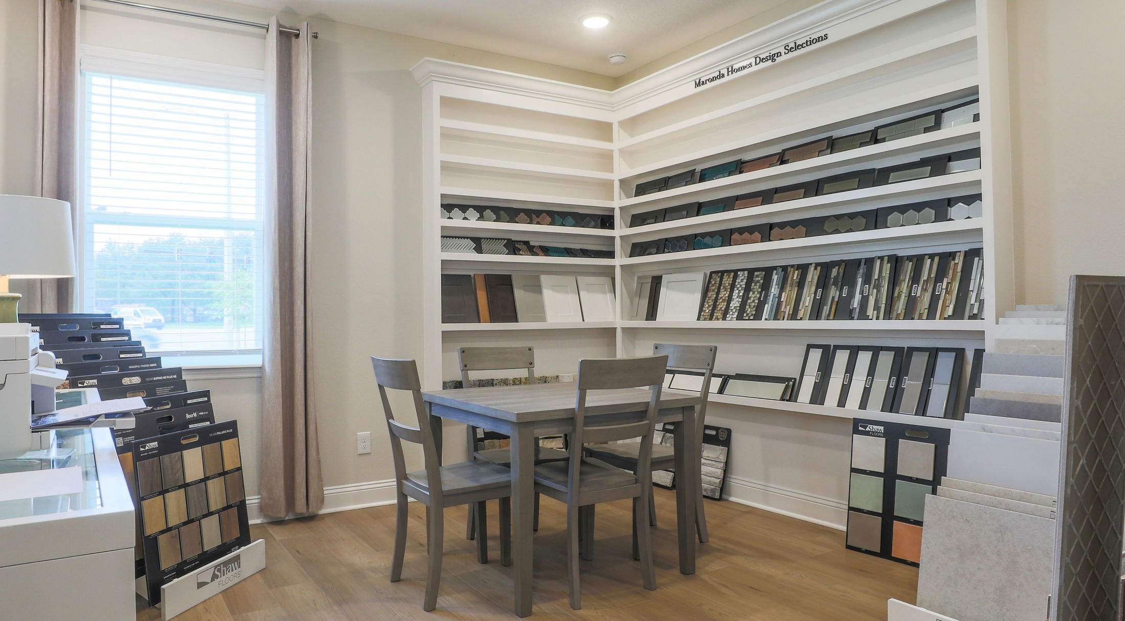 Contemporary home design studio with a table, chairs, and shelves displaying various flooring and tile samples.