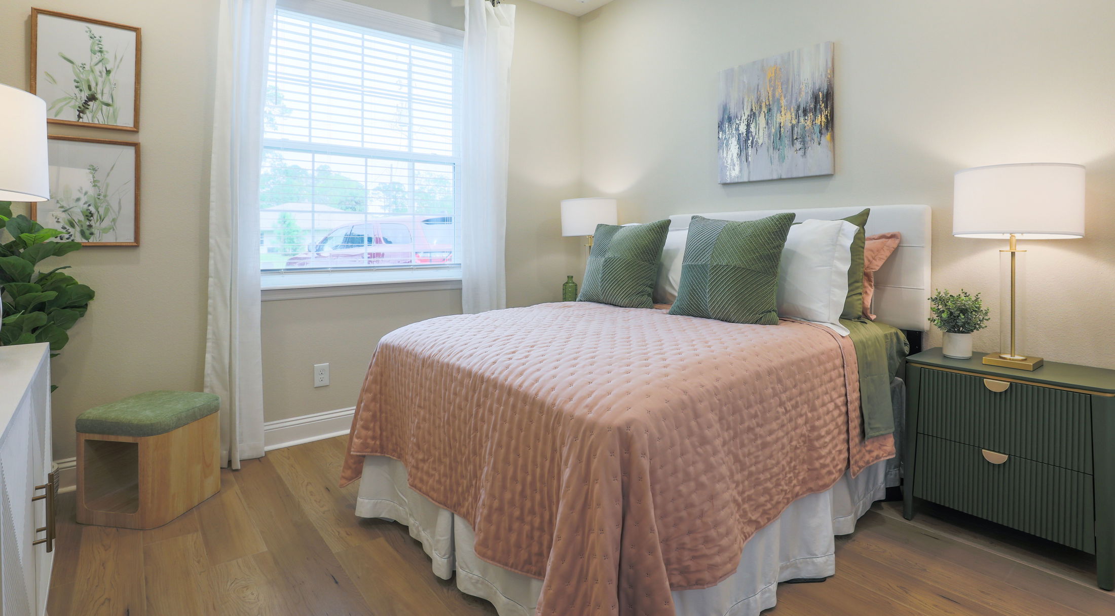 Modern bedroom with a cozy bed featuring green and pink linens, a stylish nightstand, and decorative paintings.