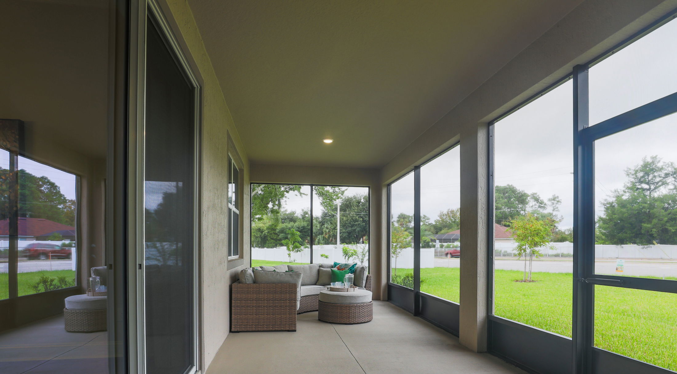 Covered patio with comfortable wicker furniture and screened windows overlooking a green lawn on a cloudy day.