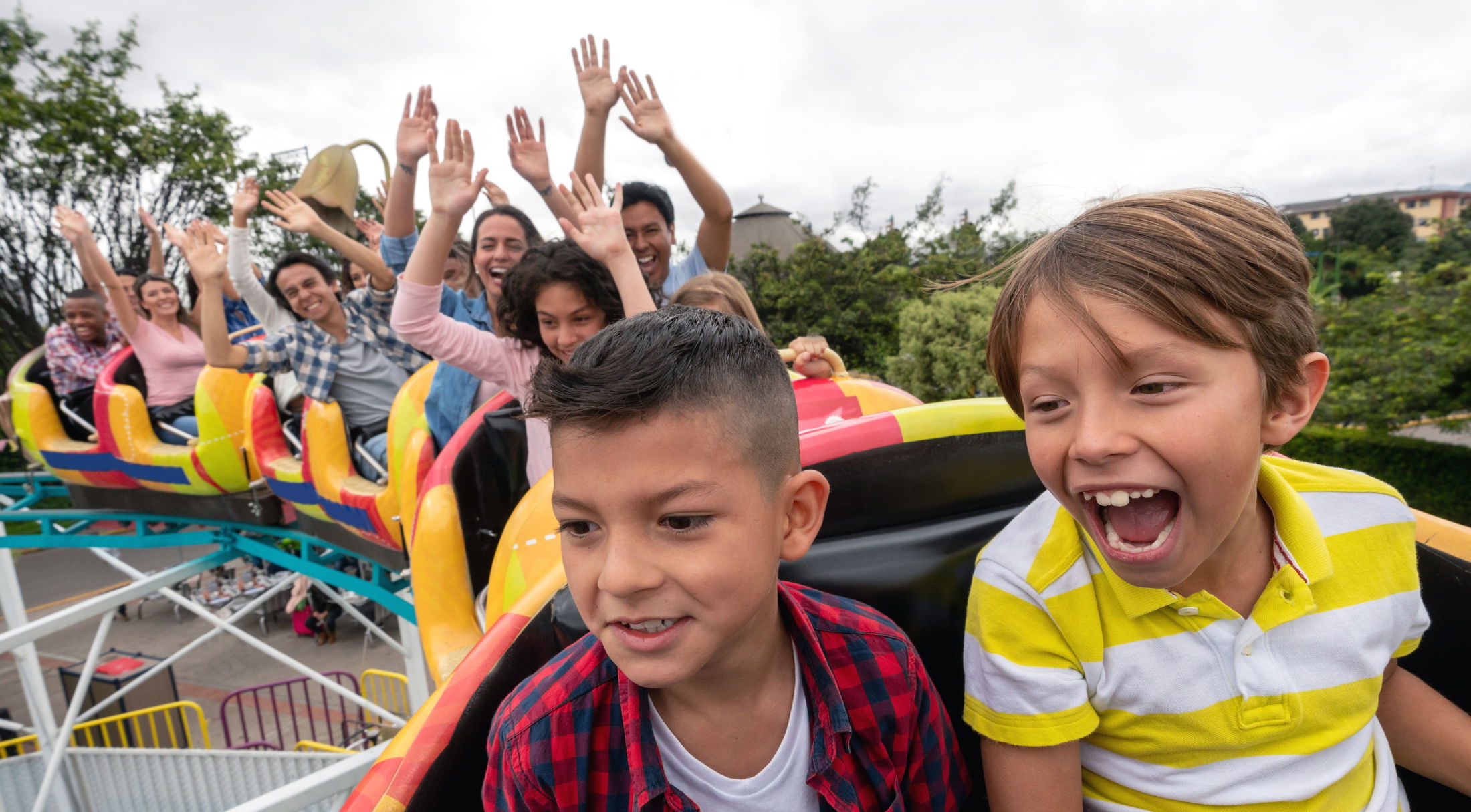 Children and adults joyfully riding a colorful roller coaster at an amusement park.